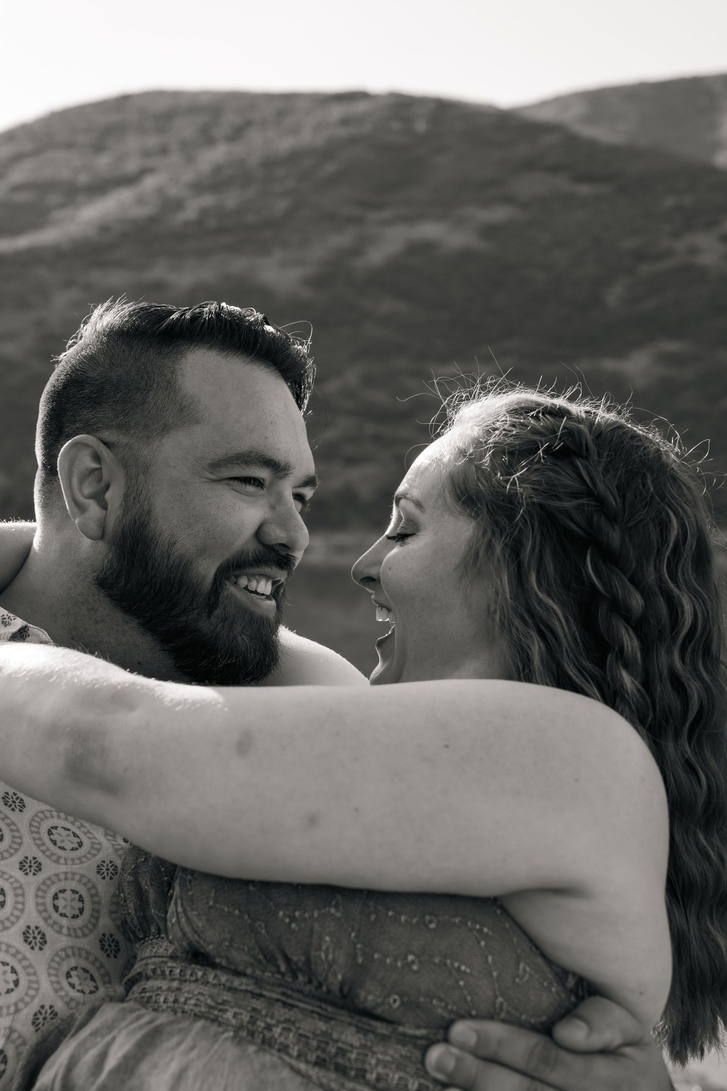 Black and white portrait of a couple laughing together with mountains in background.