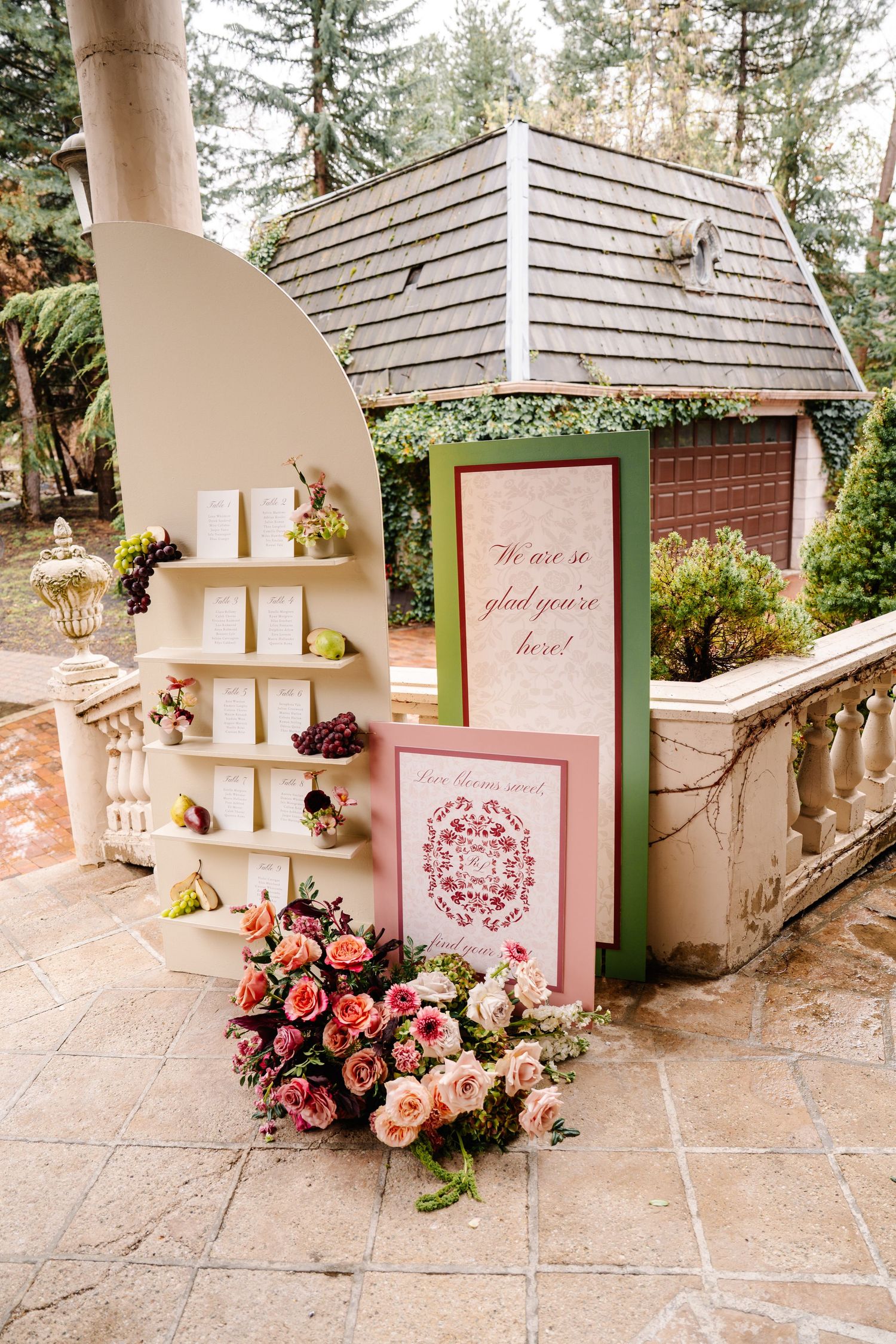 Pink floral wedding signage and roses displayed on stone balustrade at outdoor venue.