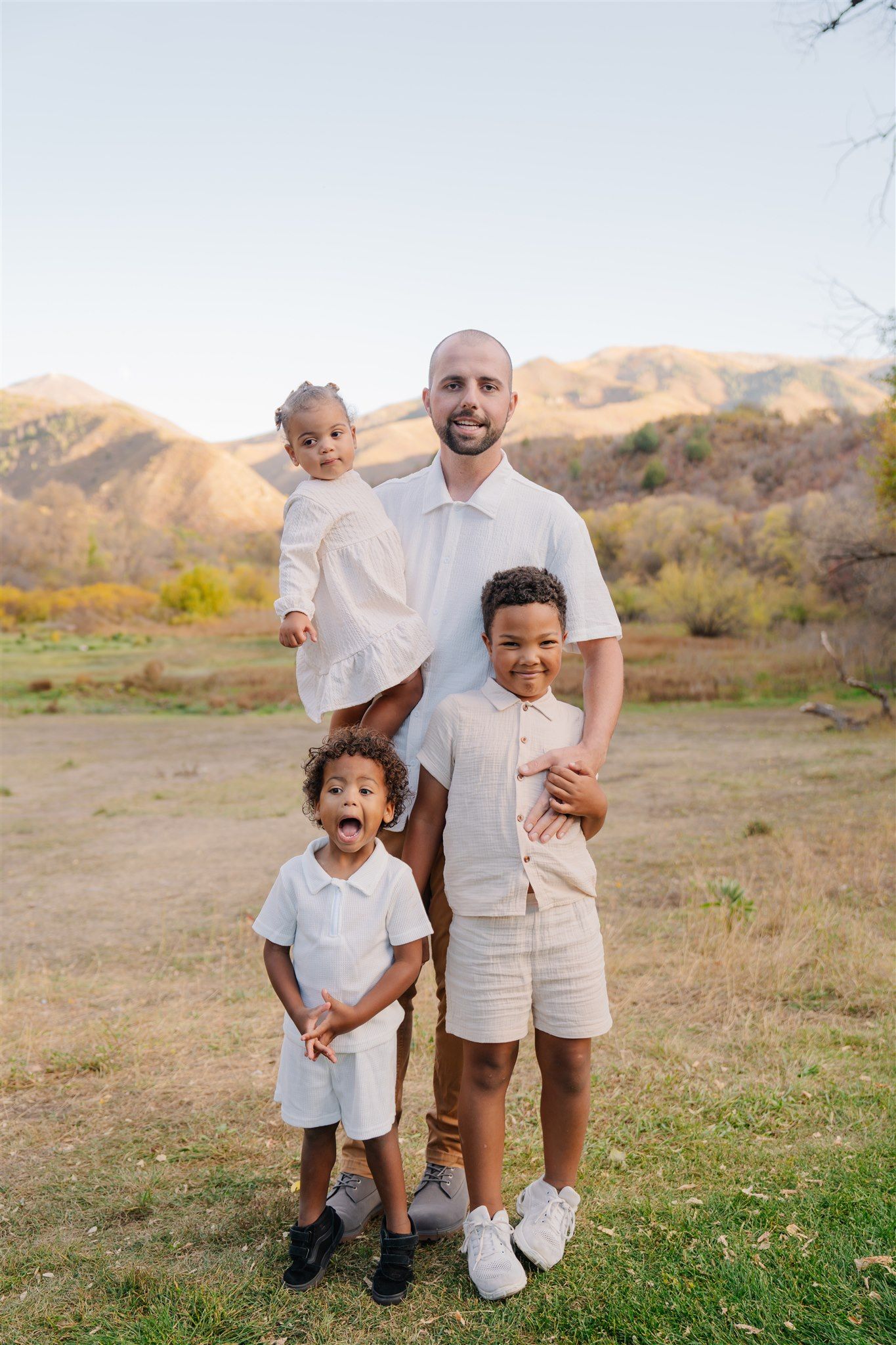 Family portrait in white and khaki outfits against a desert mountain landscape.