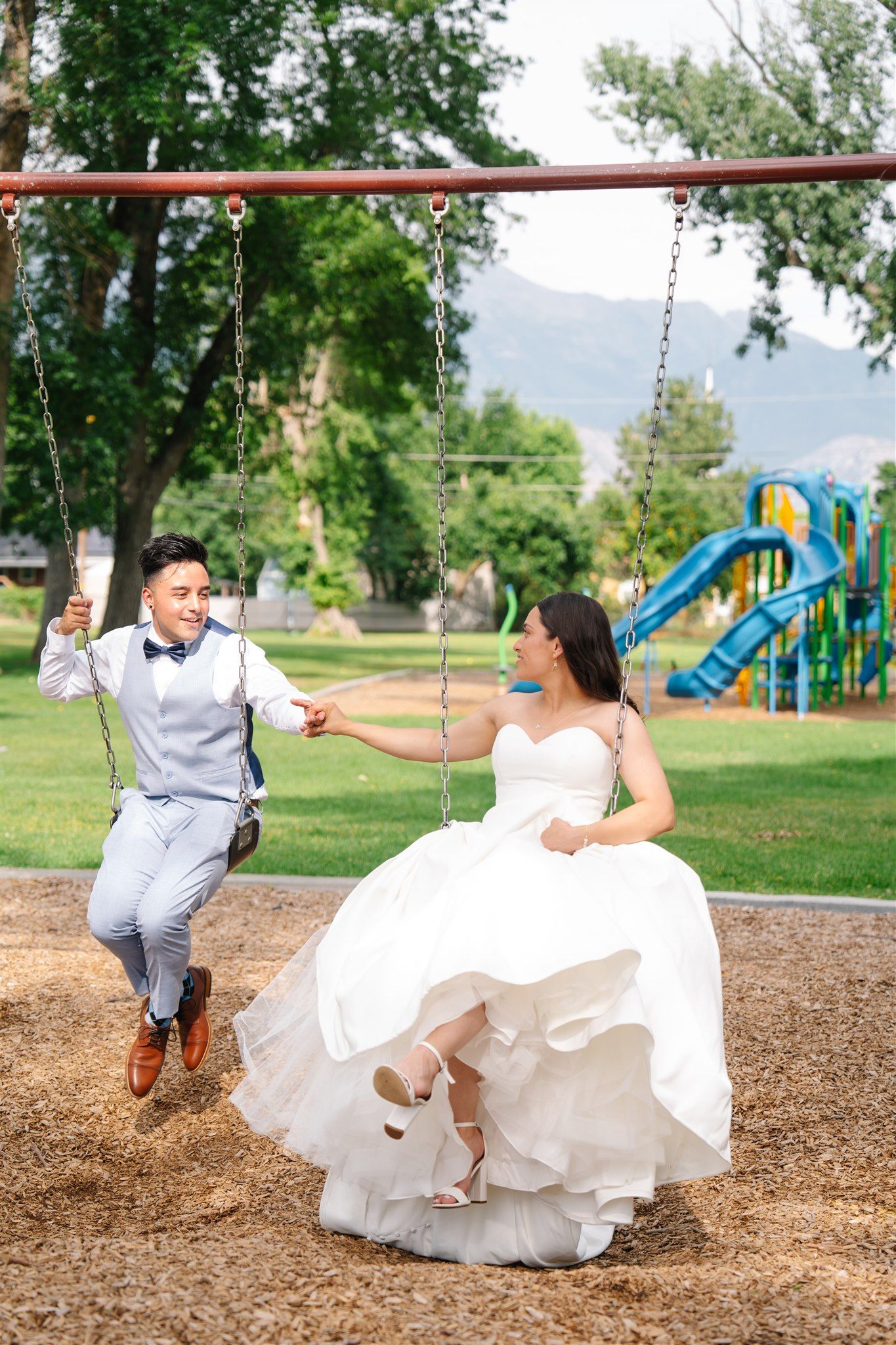 Newlyweds playing on playground swings in formal wedding attire.