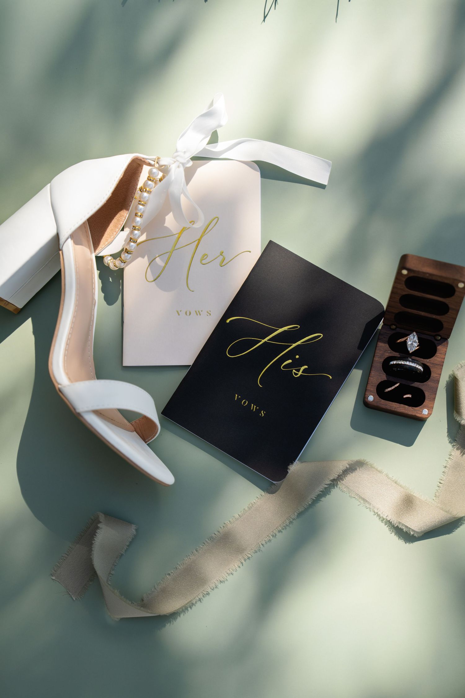Elegant wedding ring boxes and stationery arranged with delicate shadows on a light surface.
