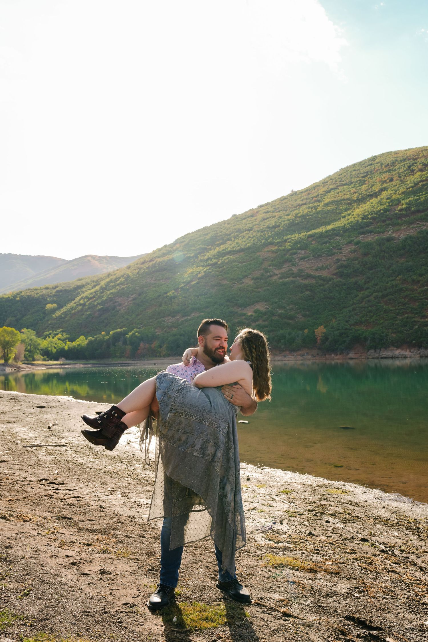 Person carrying their partner in their arms by a scenic mountain lake.