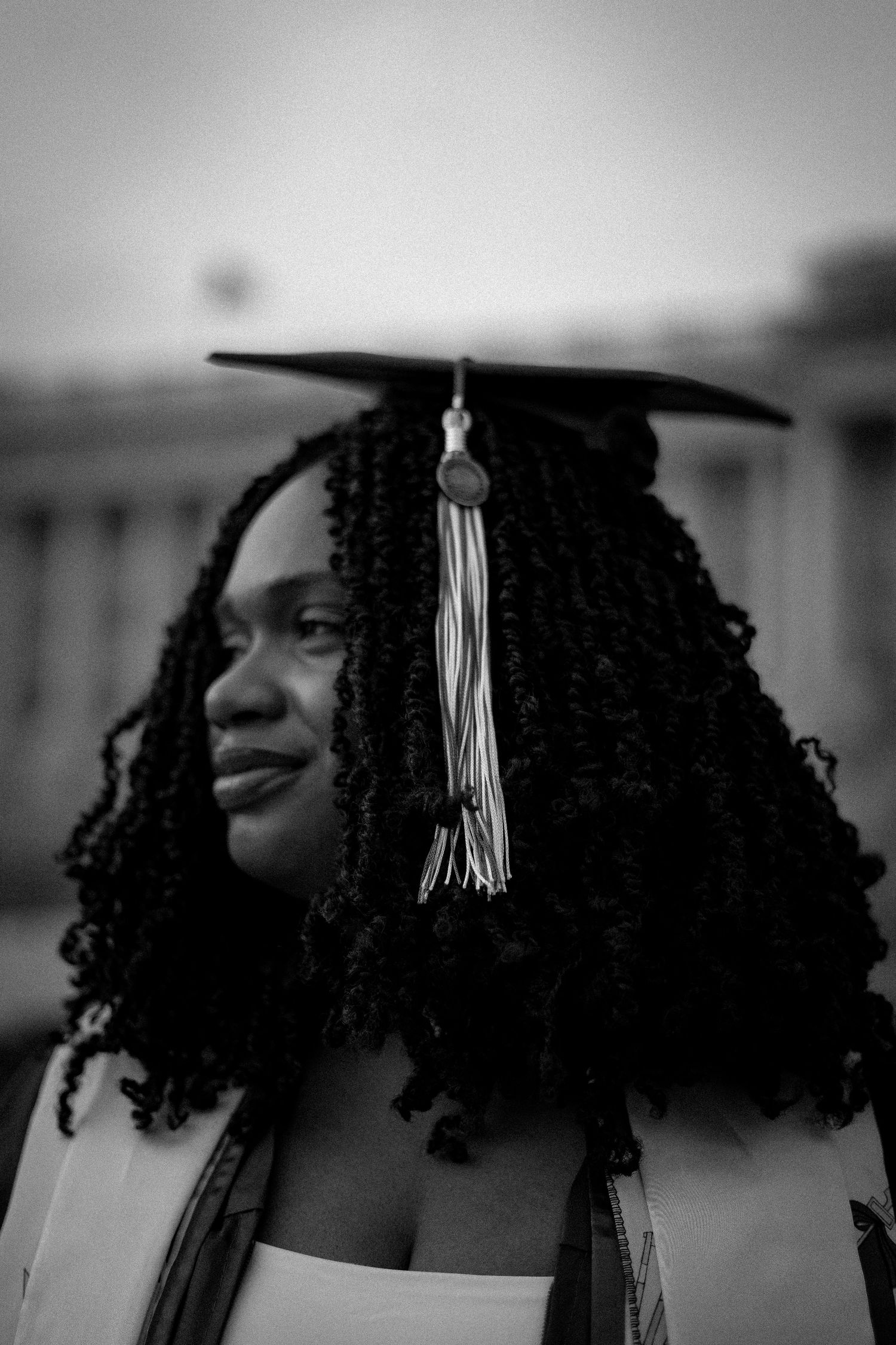 Graduate wearing mortarboard tassel poses in black and white portrait series.