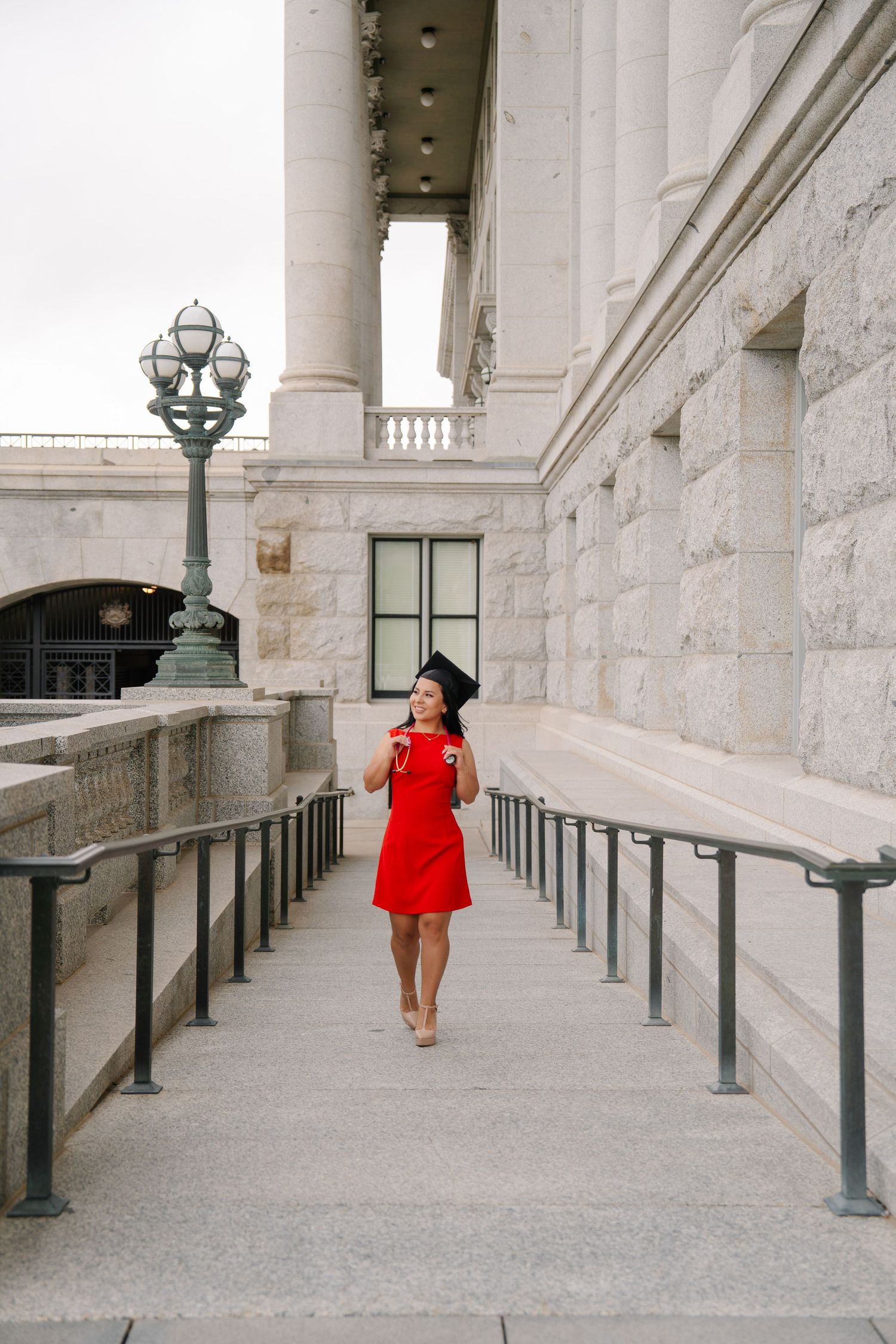 Red dress contrasts against white stone colonnade with vintage lamp posts.