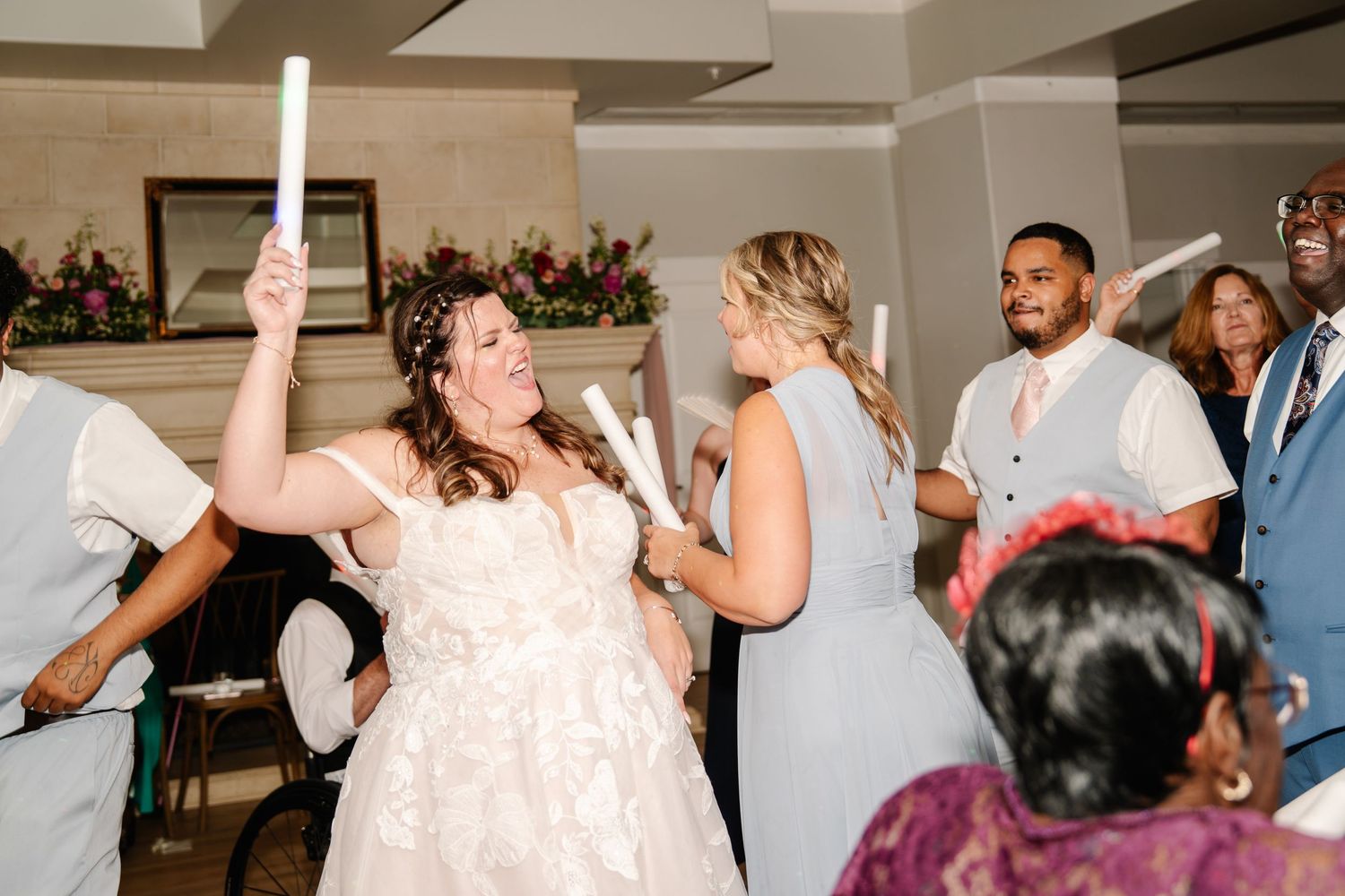 Wedding celebration with guests dancing and holding light-up wands on the dance floor.