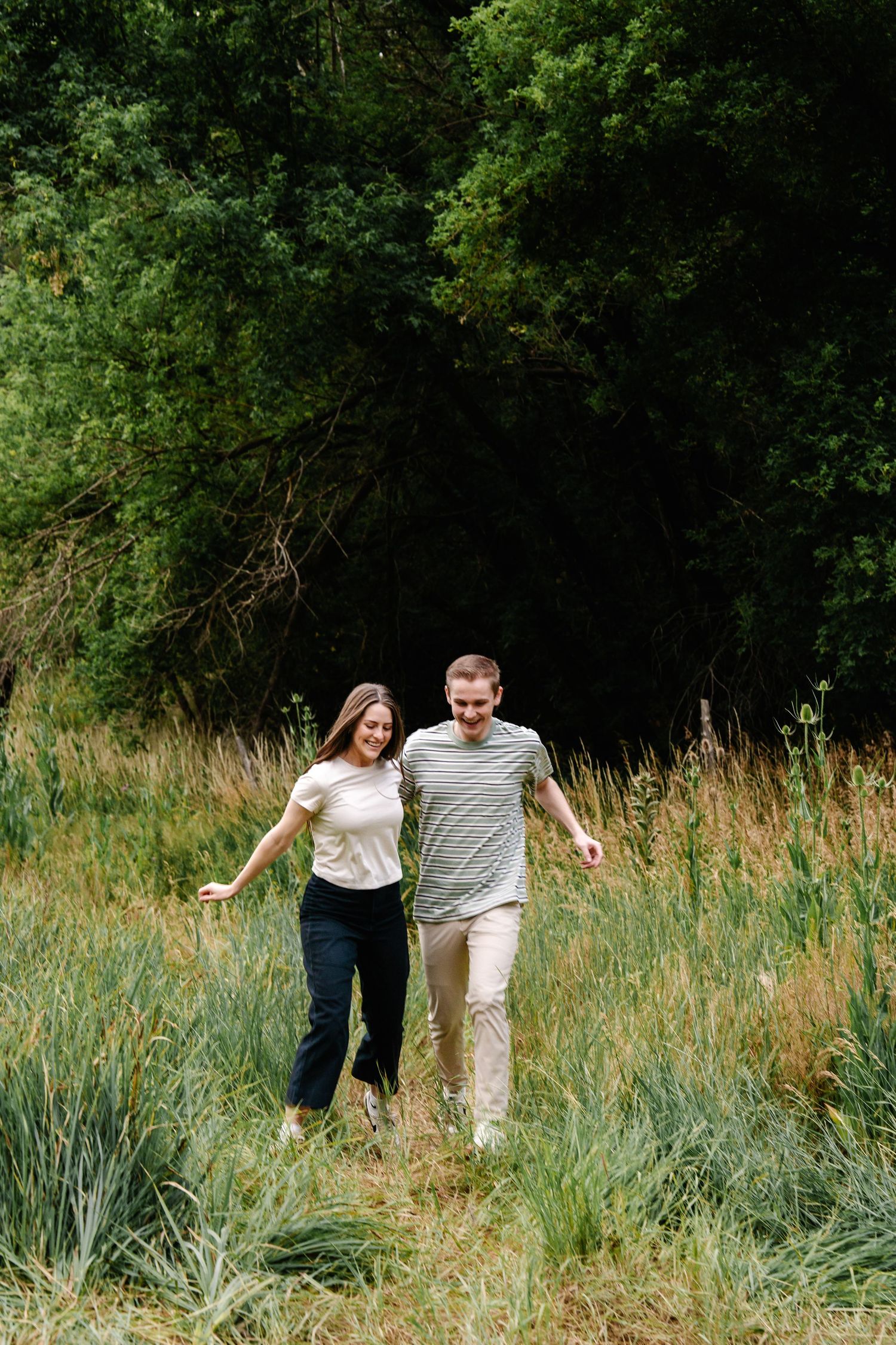 A couple walks playfully through tall grass in a natural outdoor setting.