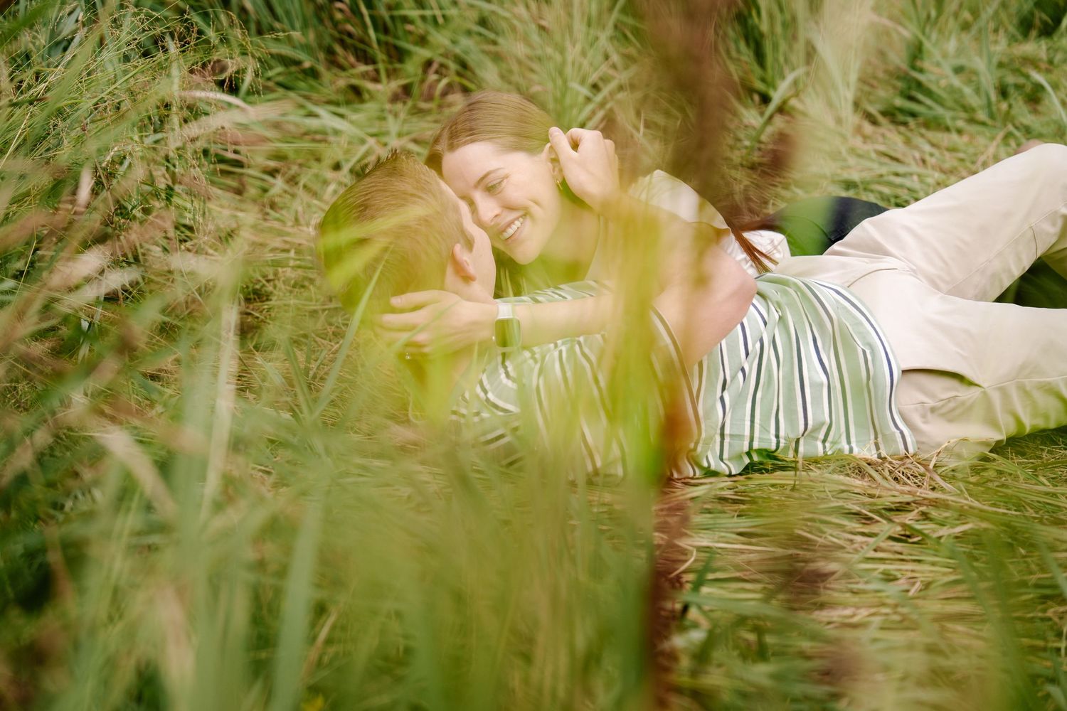 Couple lying in tall grass during golden hour photoshoot.