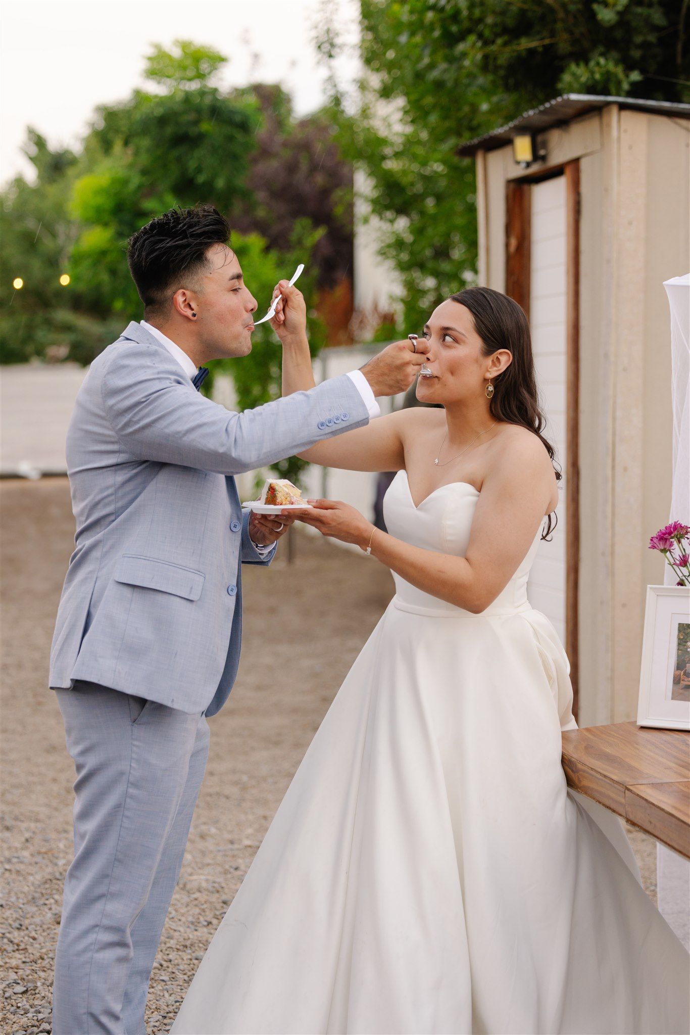 Playful wedding couple sharing cake during their reception celebration.