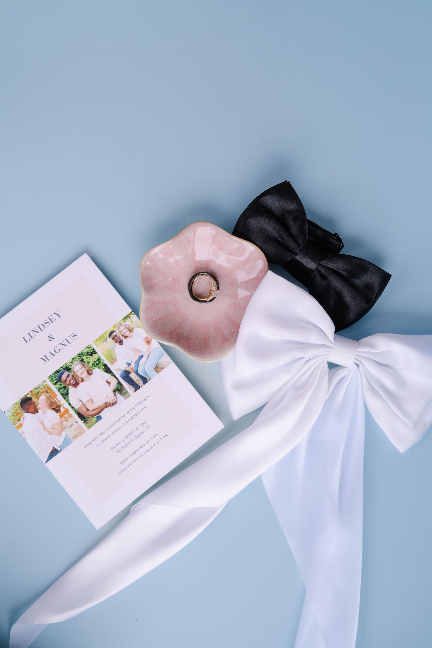 Wedding stationery and white bow arranged on light blue background.