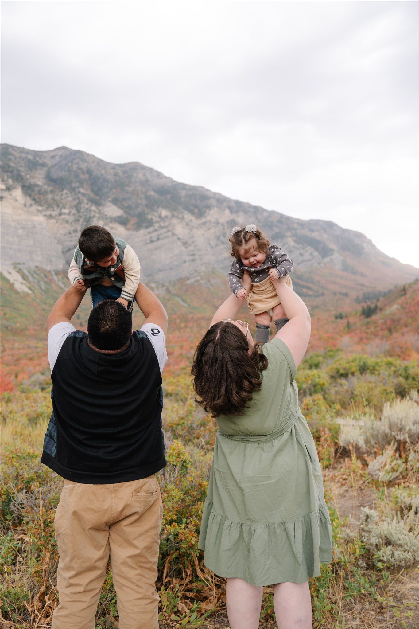 Two people in casual wear standing against mountain backdrop during autumn.