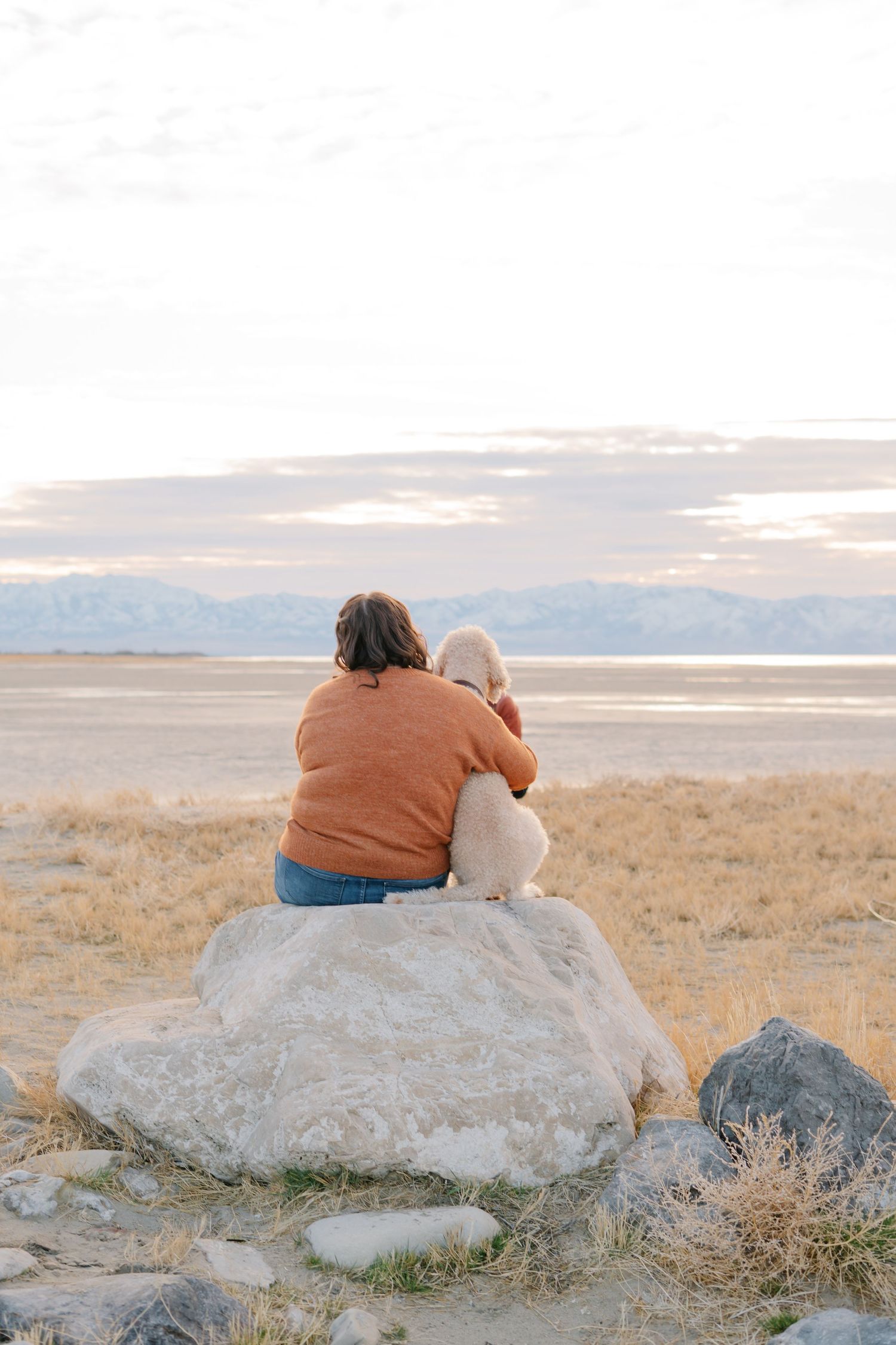 Two people sitting together on a large rock formation at sunset overlooking a scenic landscape.