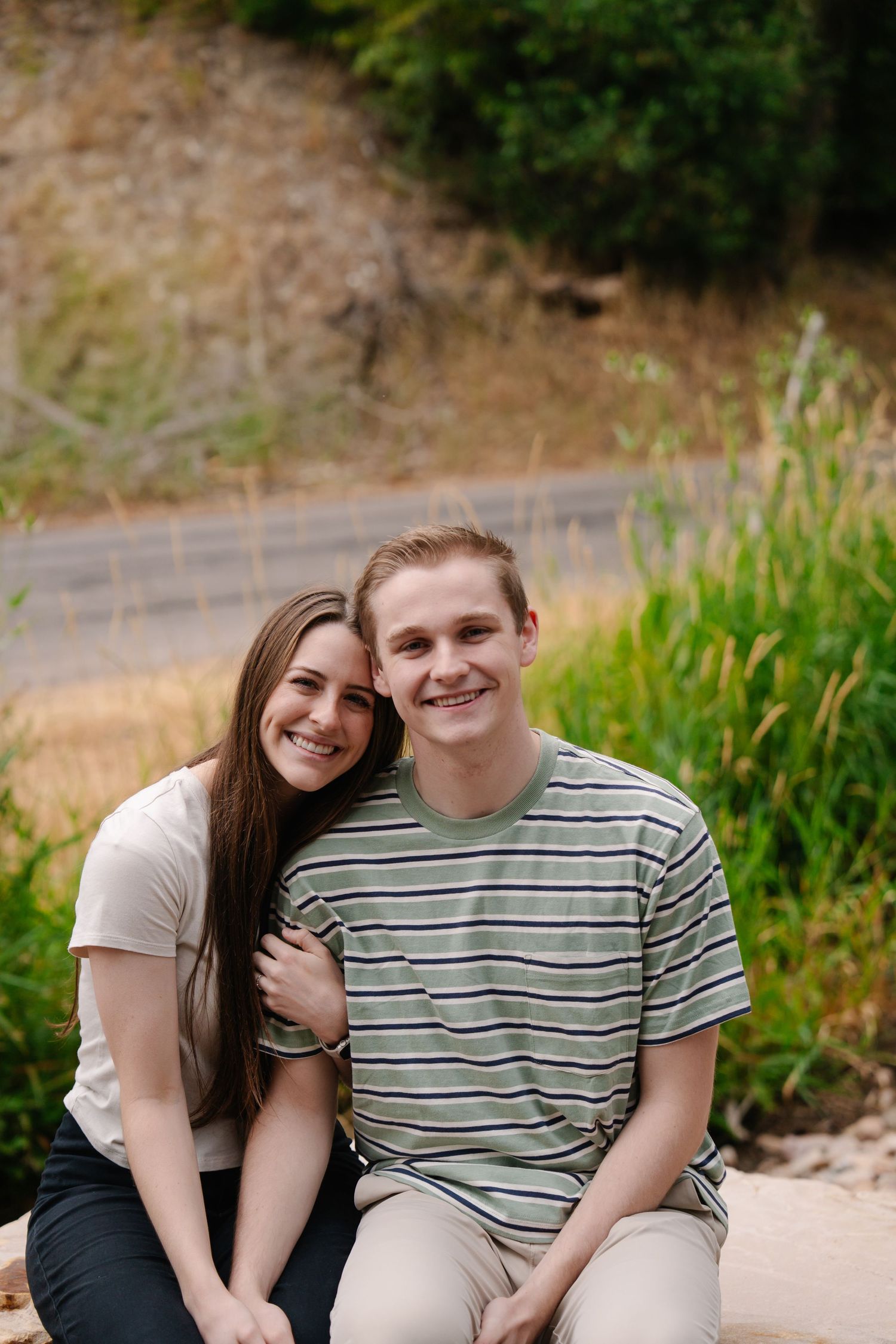 Couple sitting together on ground with mountains in background.