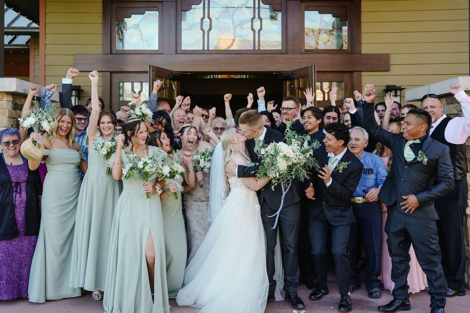 Large wedding party poses together outside venue with guests holding sparklers in celebration.
