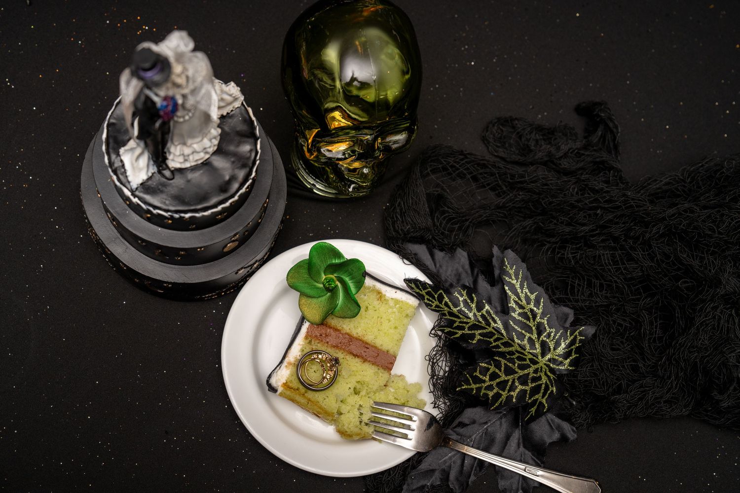 Gothic wedding display with skull bottle, bride figurine, and a slice of cake on a plate with dark lace decor.