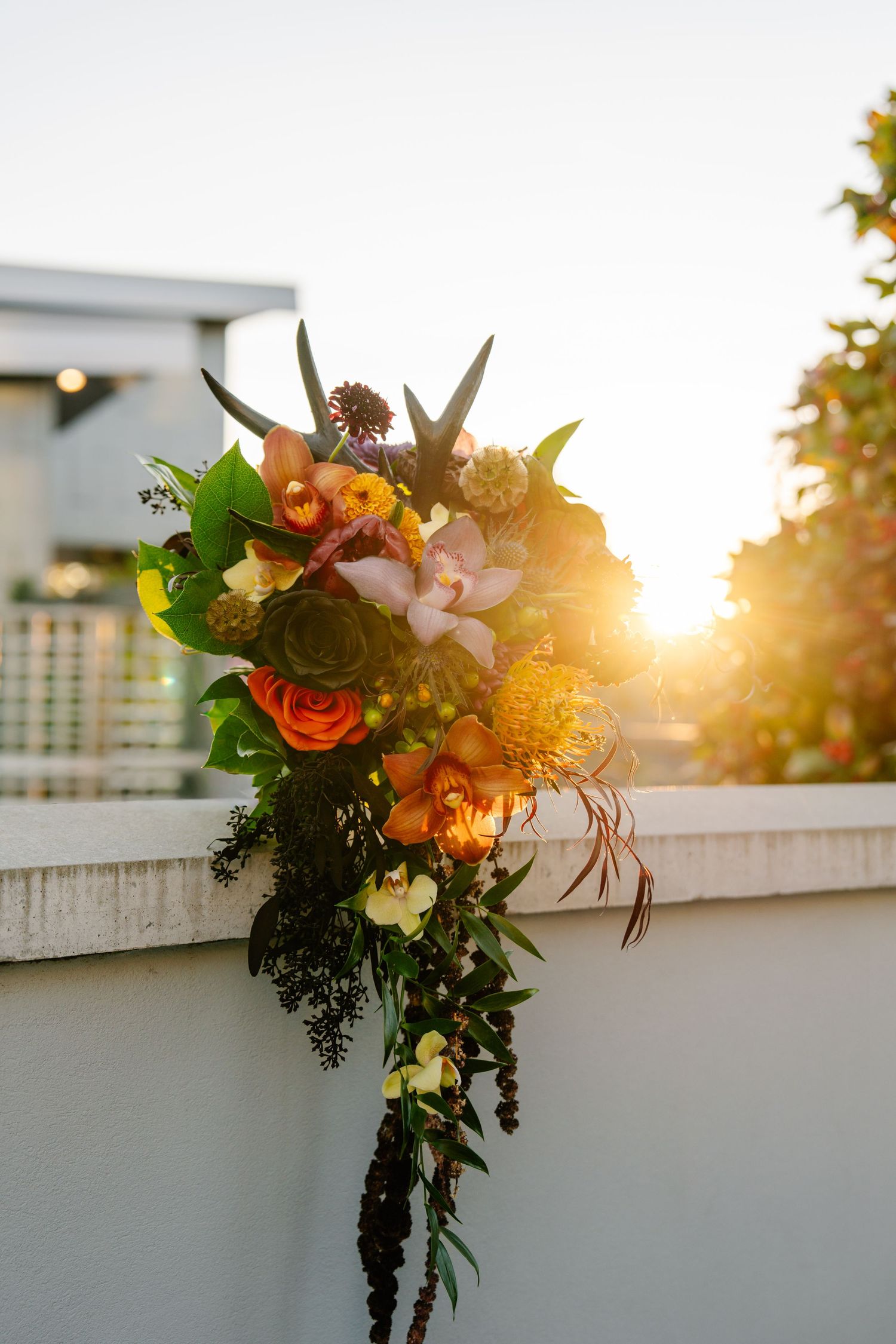 Vibrant floral bouquet with orange roses and mixed flowers against sunset sky.
