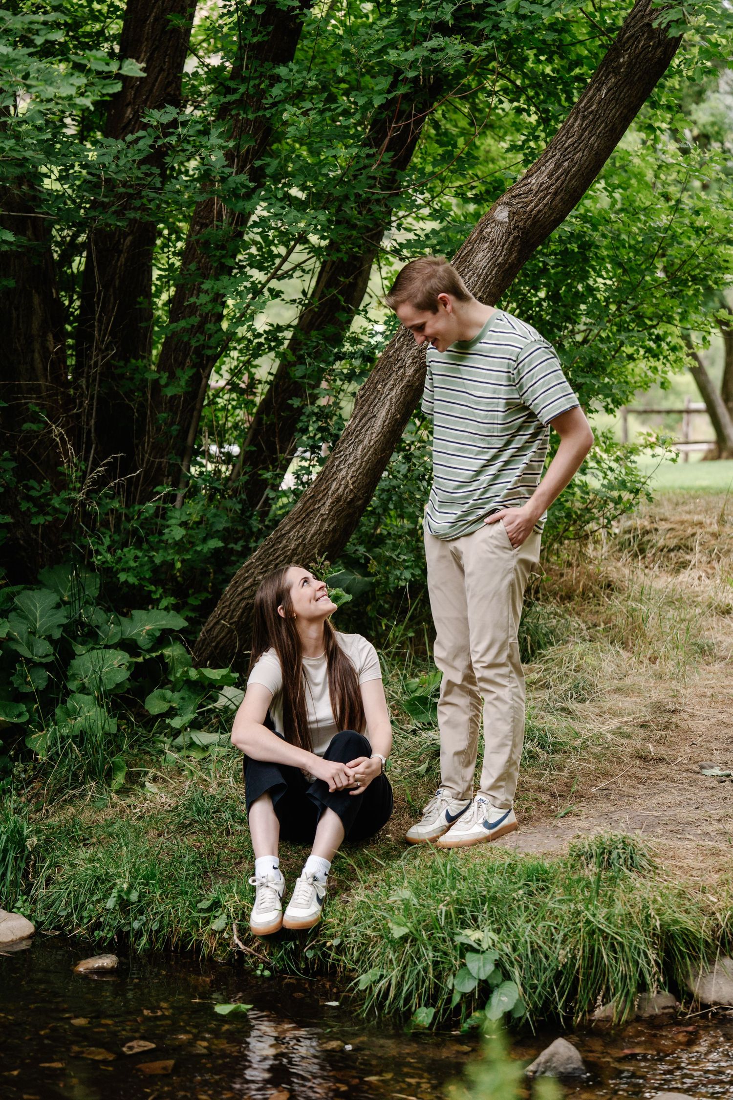 Two people explore a creek bed surrounded by lush greenery.
