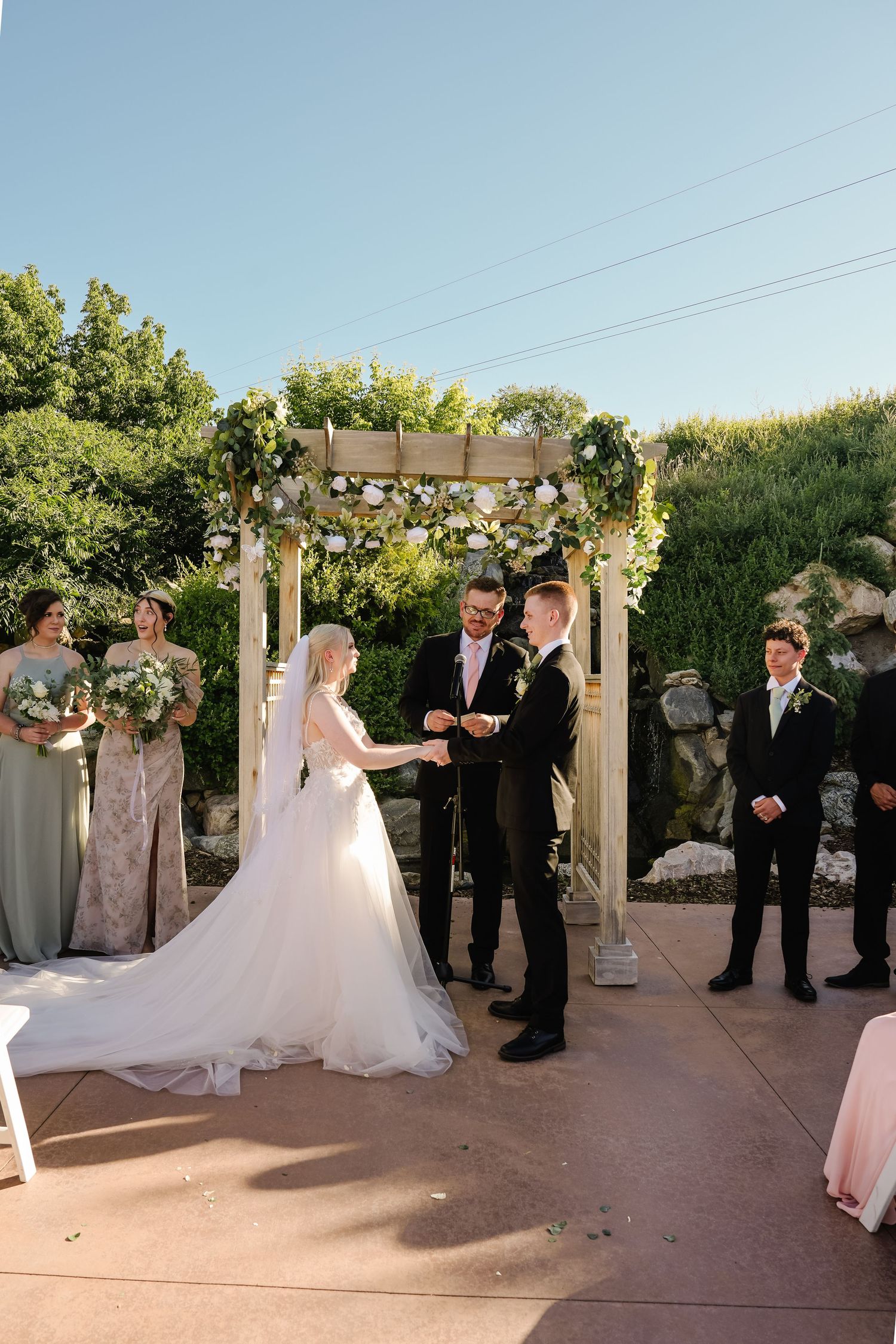 Outdoor wedding ceremony under floral arch with wedding party.
