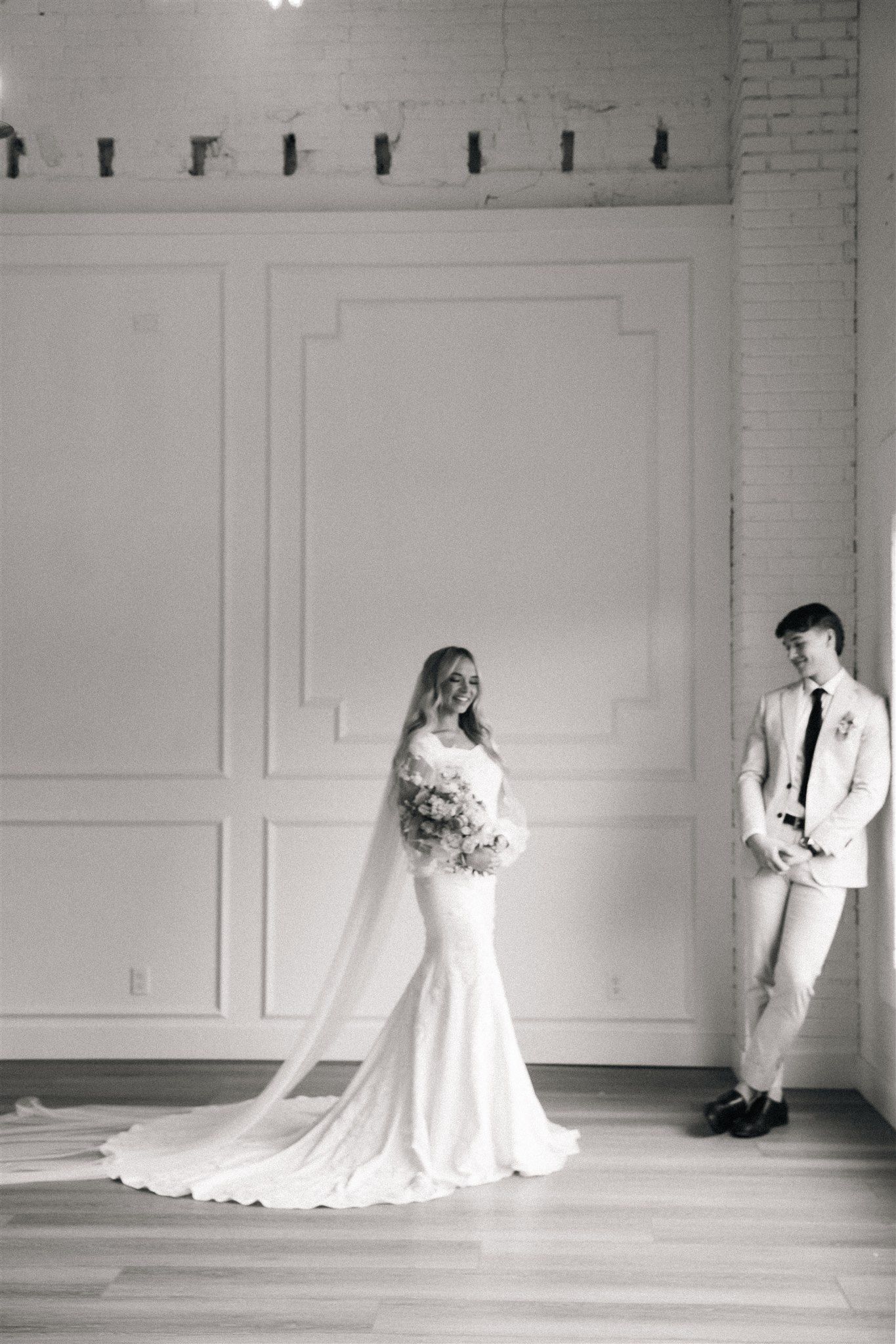 Artistic black and white wedding portraits against a white brick wall.