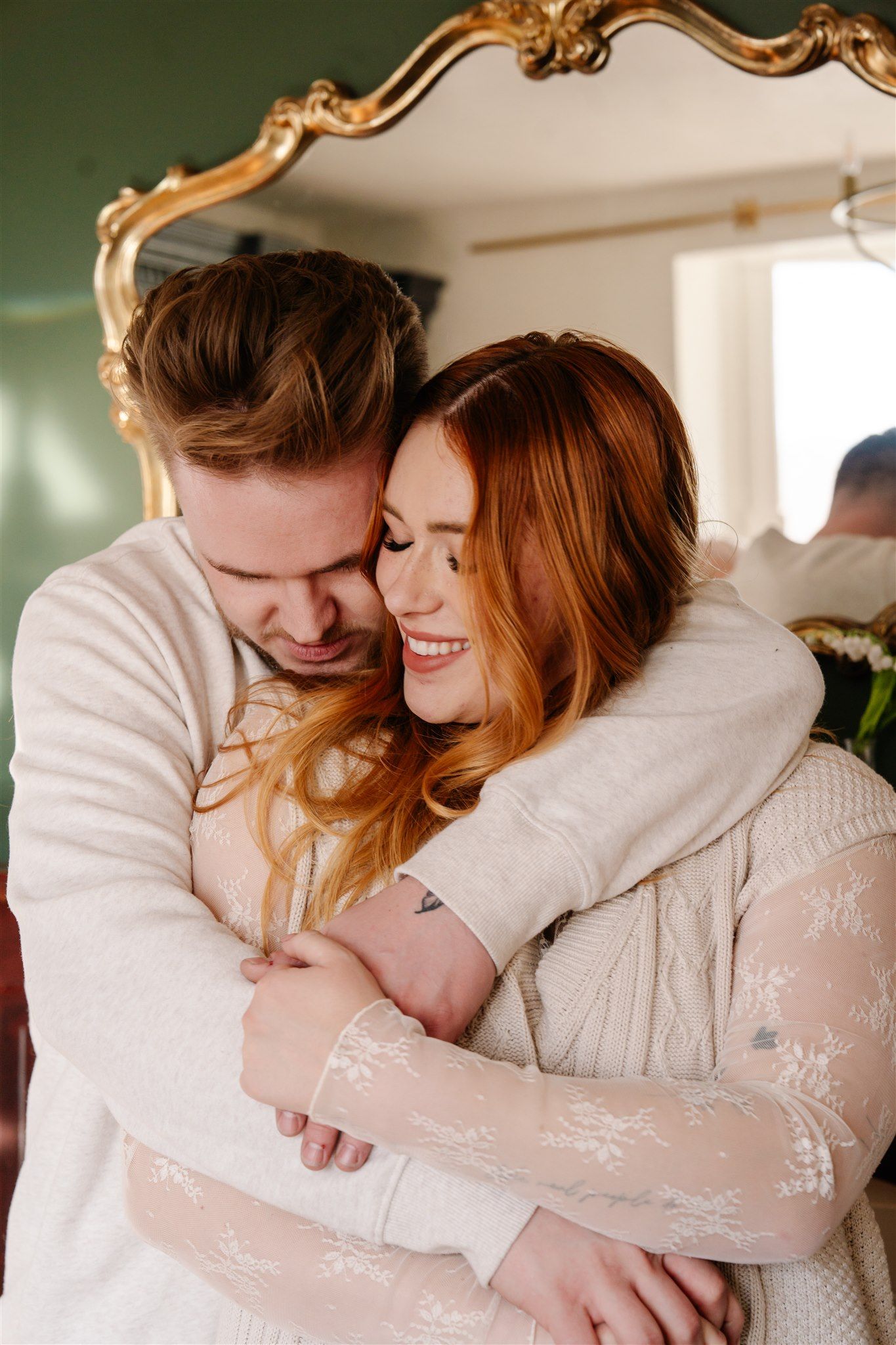 Intimate couple embracing in a room with ornate gold mirror and green walls.