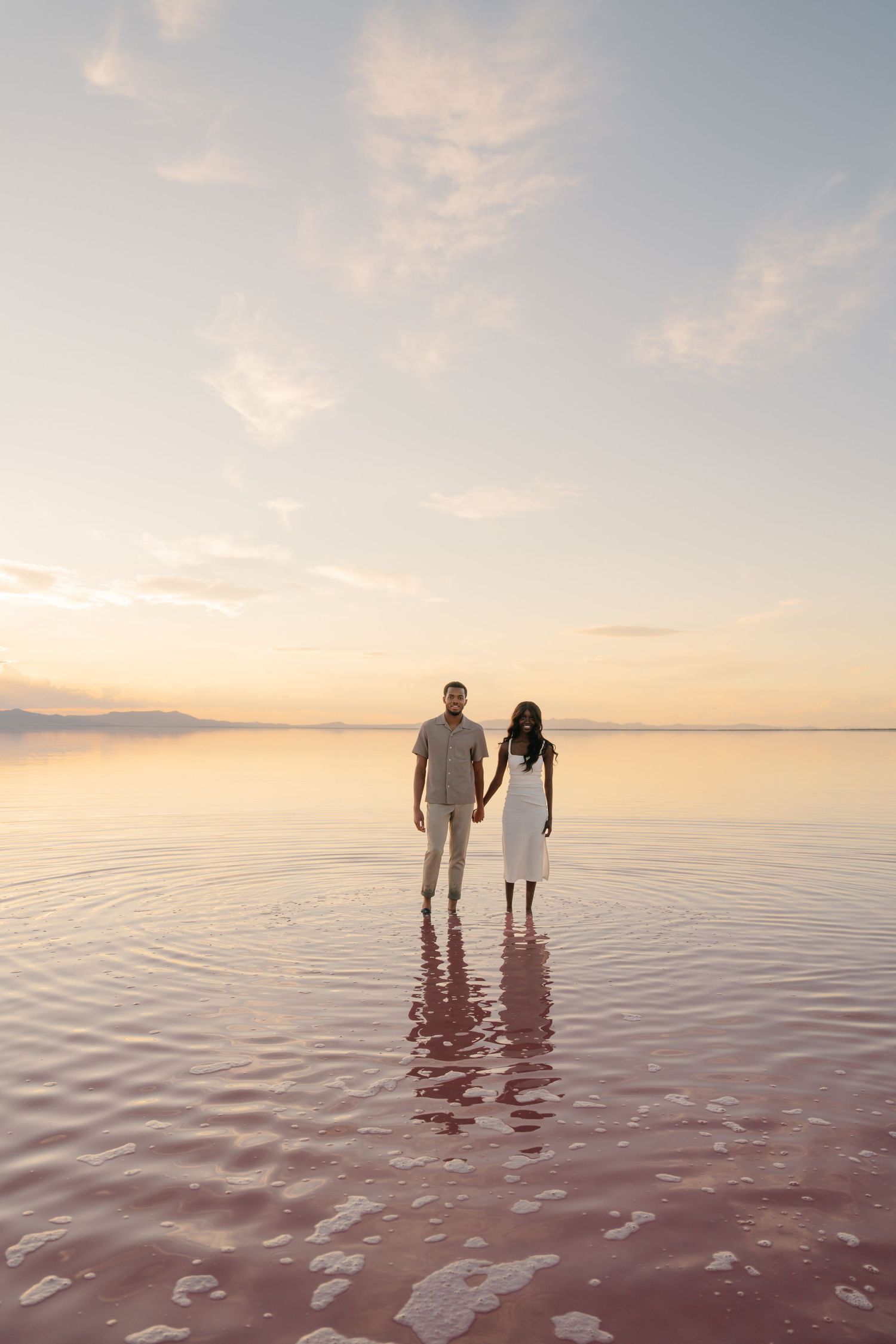 Two people stand in reflective salt water during a golden sunset.