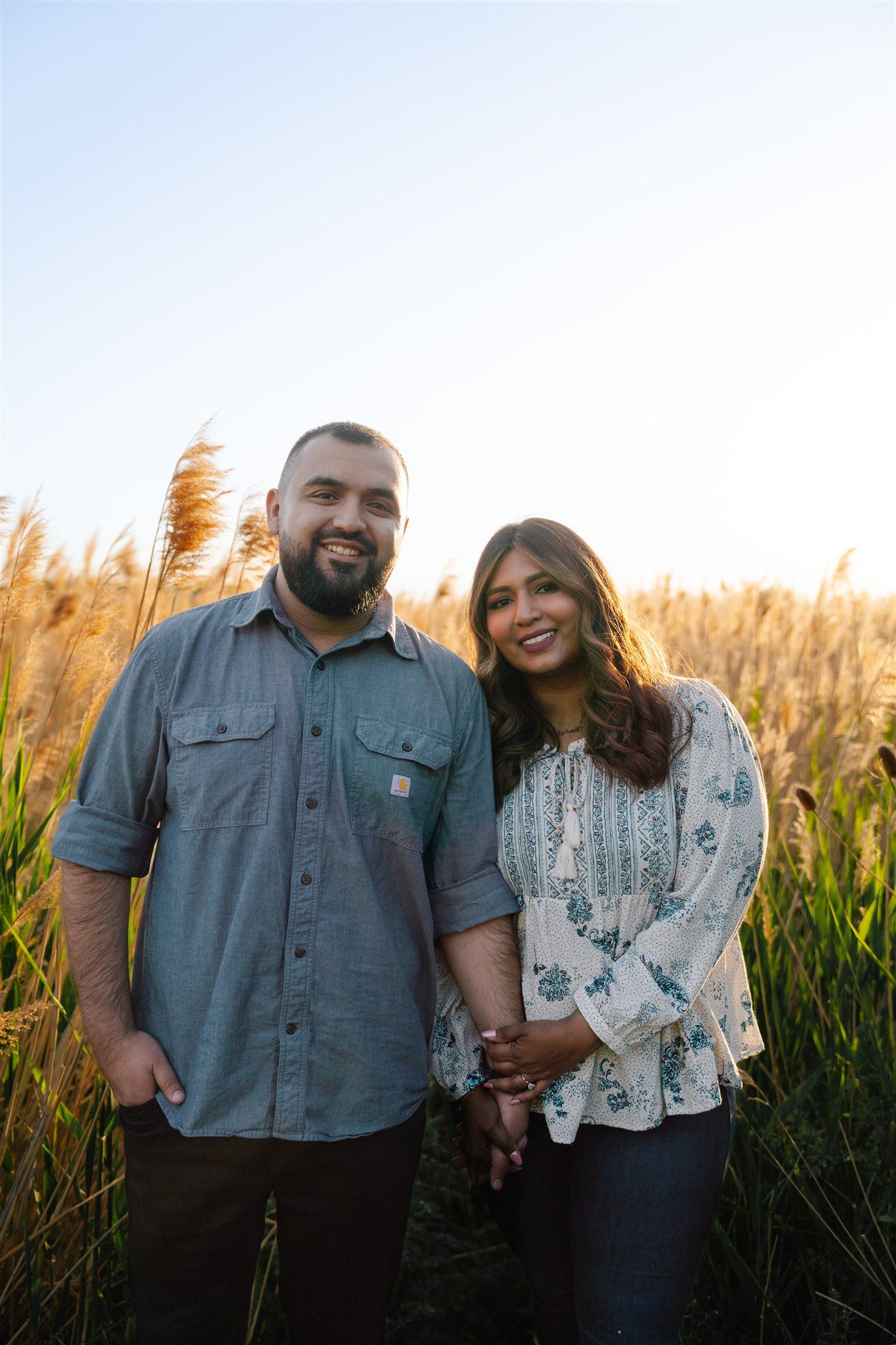 Couple standing together at sunset in field of tall grass and golden light.