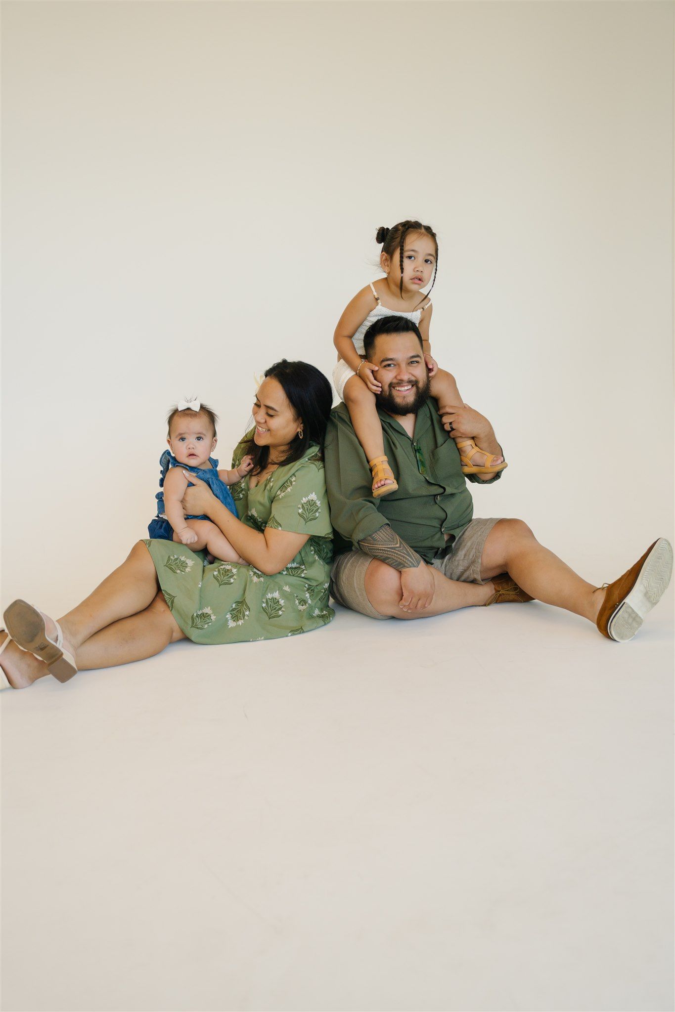 Family lying together on white background in coordinated green and neutral outfits.