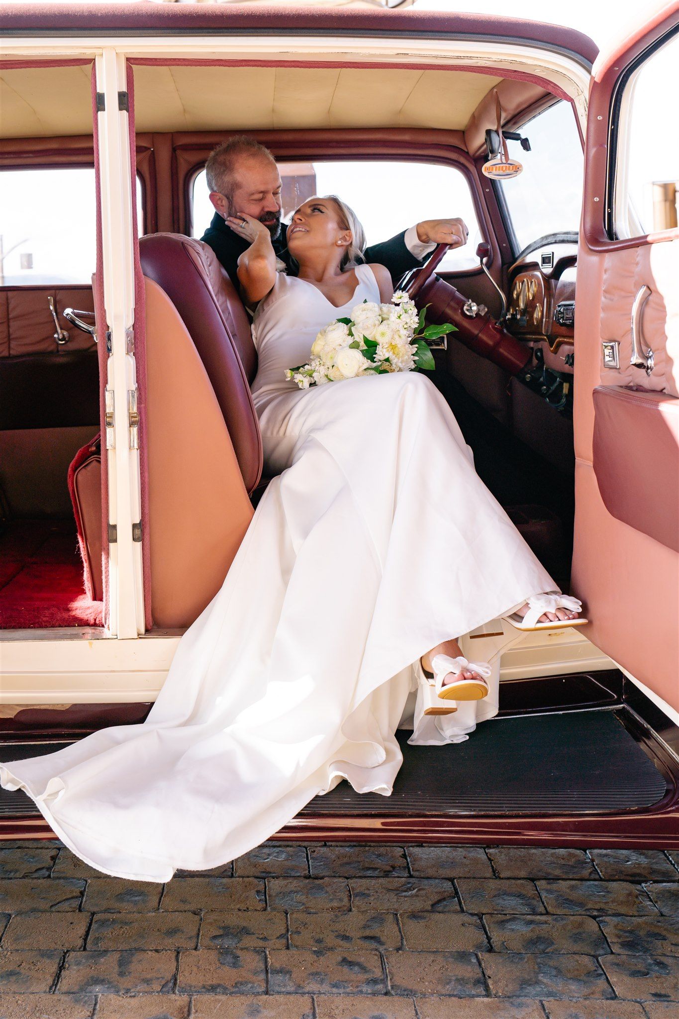 Wedding couple poses romantically in vintage pink car interior.