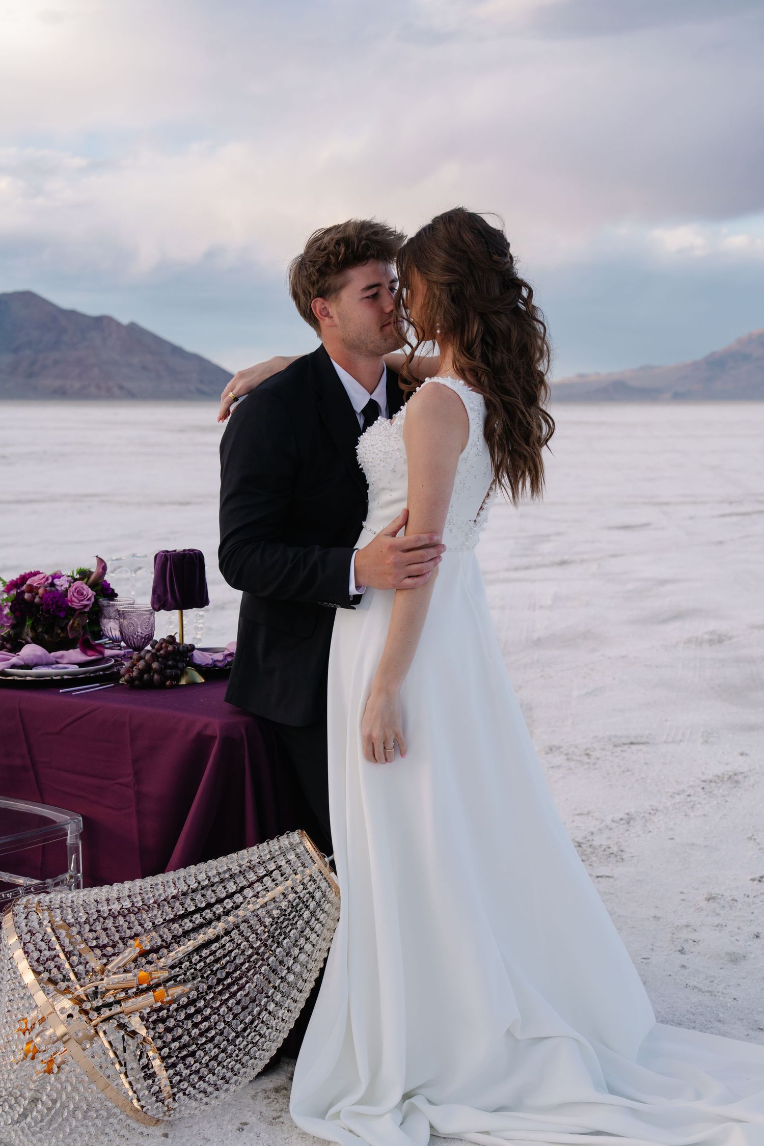 Bride and groom sharing a kiss at a stunning salt flat wedding with purple table decor and mountain backdrop.