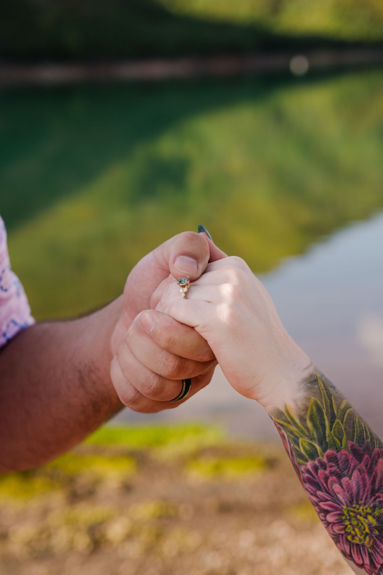 Close-up of hands with tattoos holding each other against a blurred nature background.