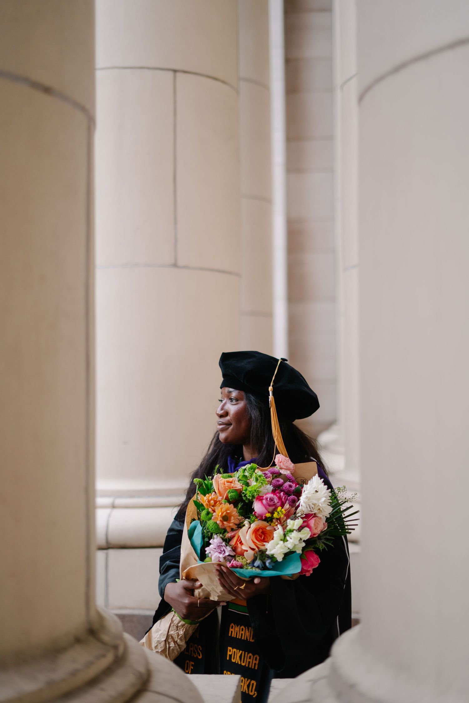 A graduation bouquet with colorful flowers held against a white column background.
