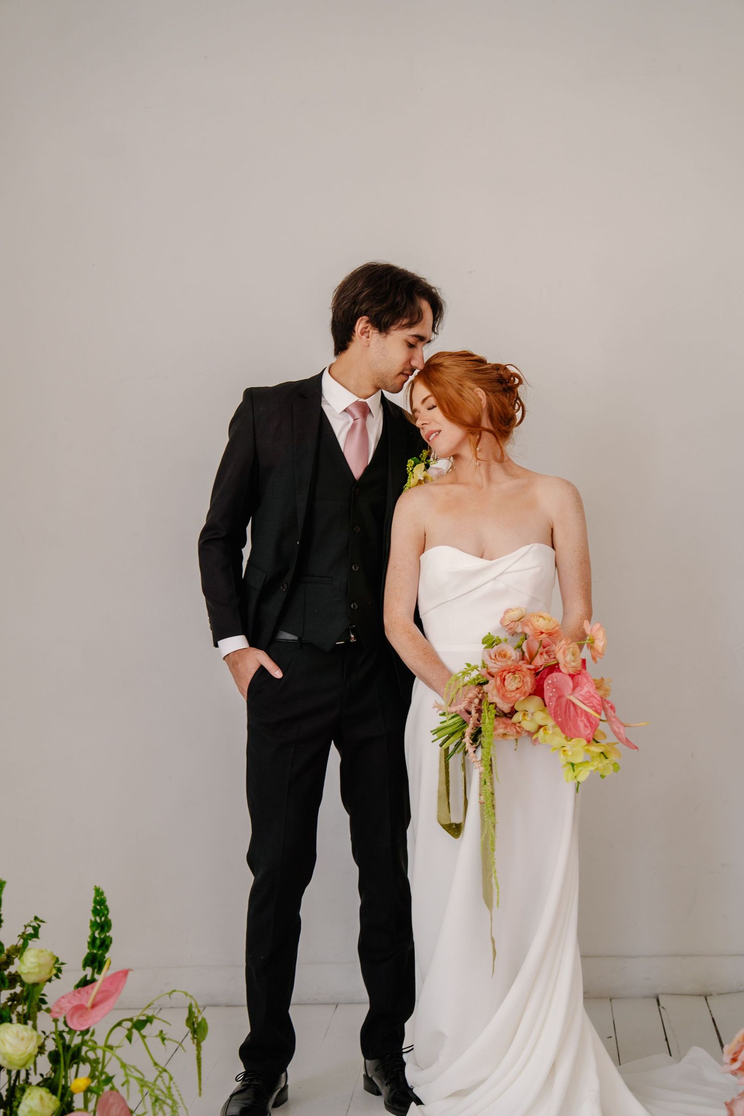Wedding couple in formal attire sharing an intimate moment against a neutral background.