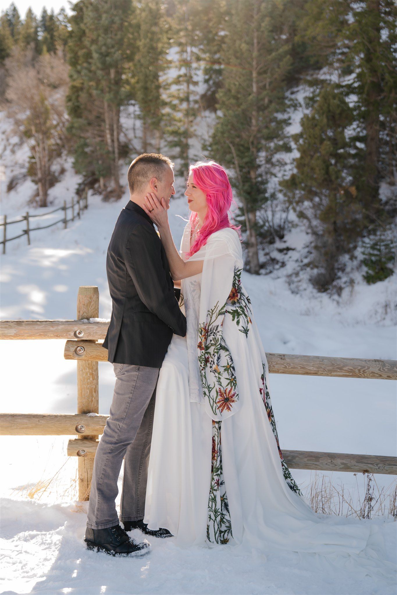 A romantic winter wedding photoshoot in a snowy mountain setting with evergreen trees in the background.