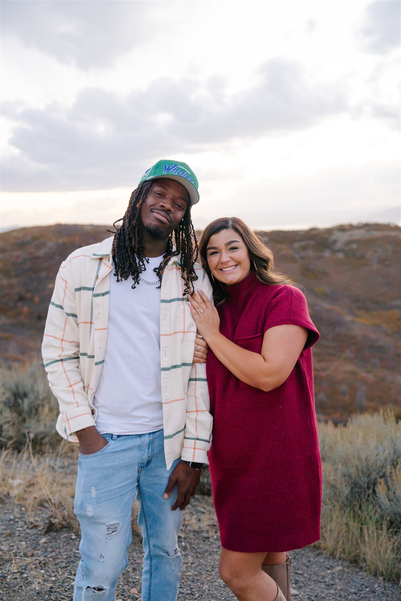 Couple laughing together outdoors against desert landscape in casual attire.