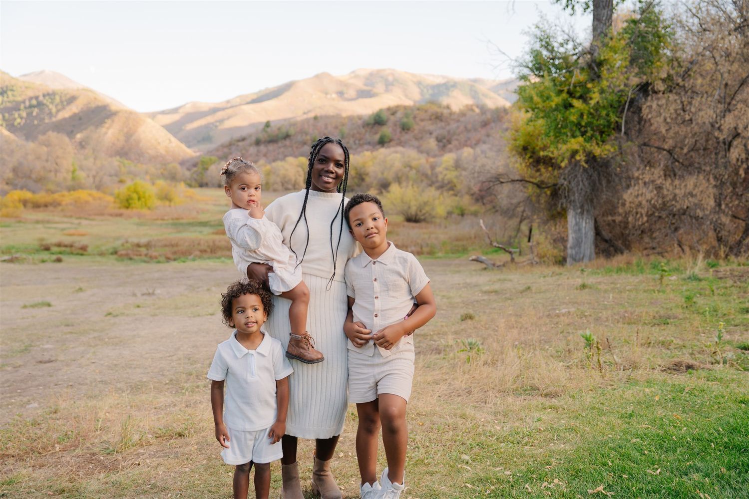 Family members sit together outdoors on a grassy hill with mountains in the background.