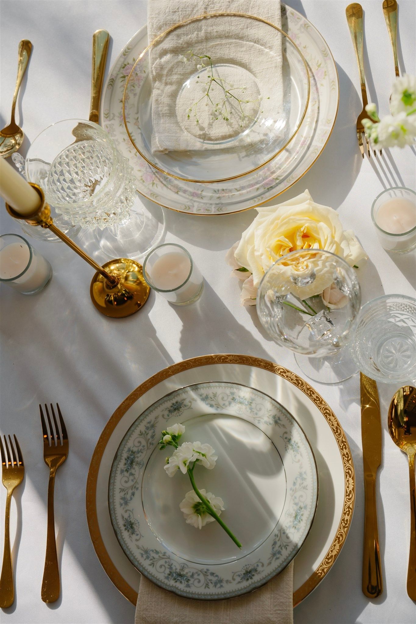Elegant table setting with gold cutlery, crystal glasses and vintage china plates.
