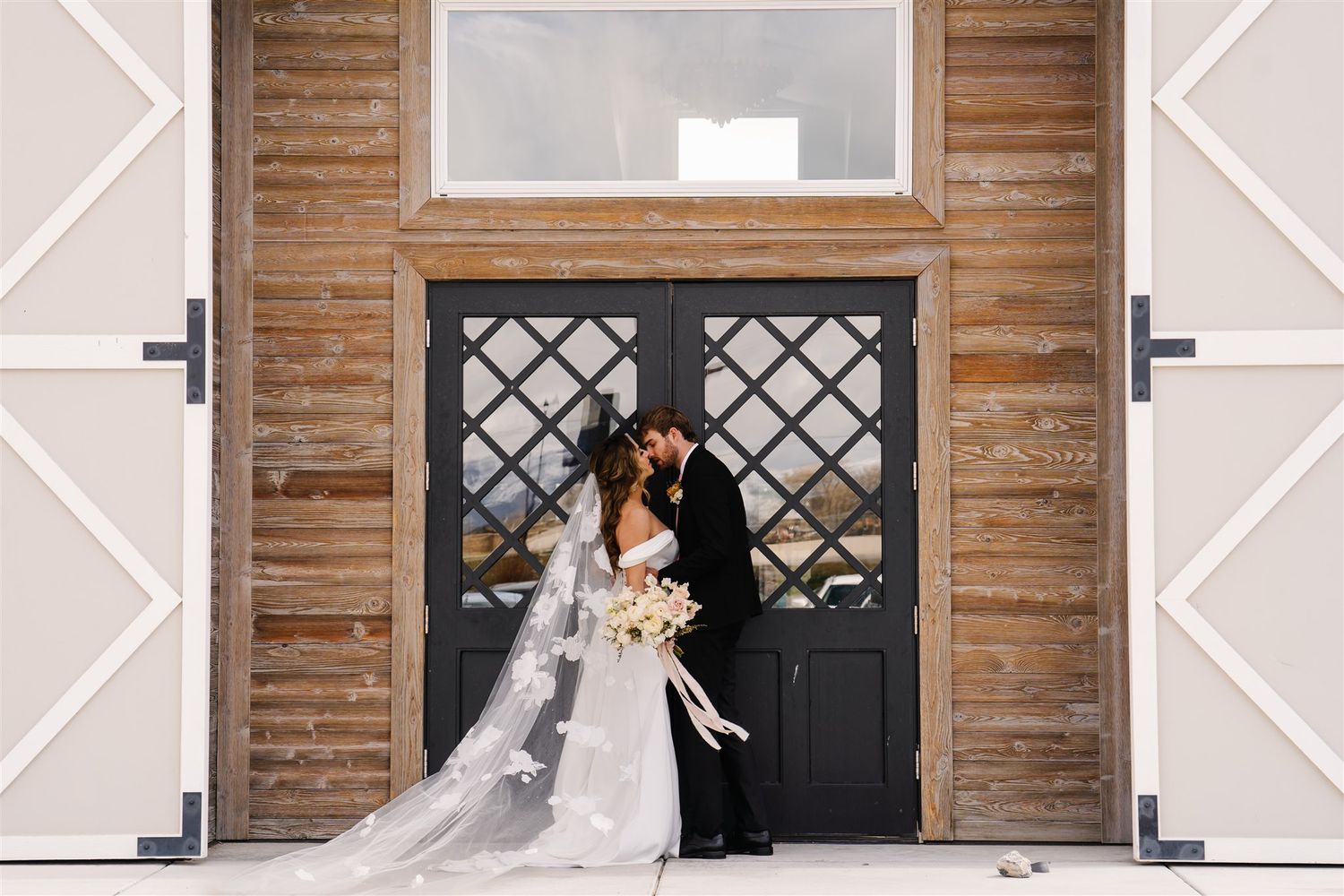 Newlyweds kissing outside modern barn venue – Salt Lake City wedding photographer.