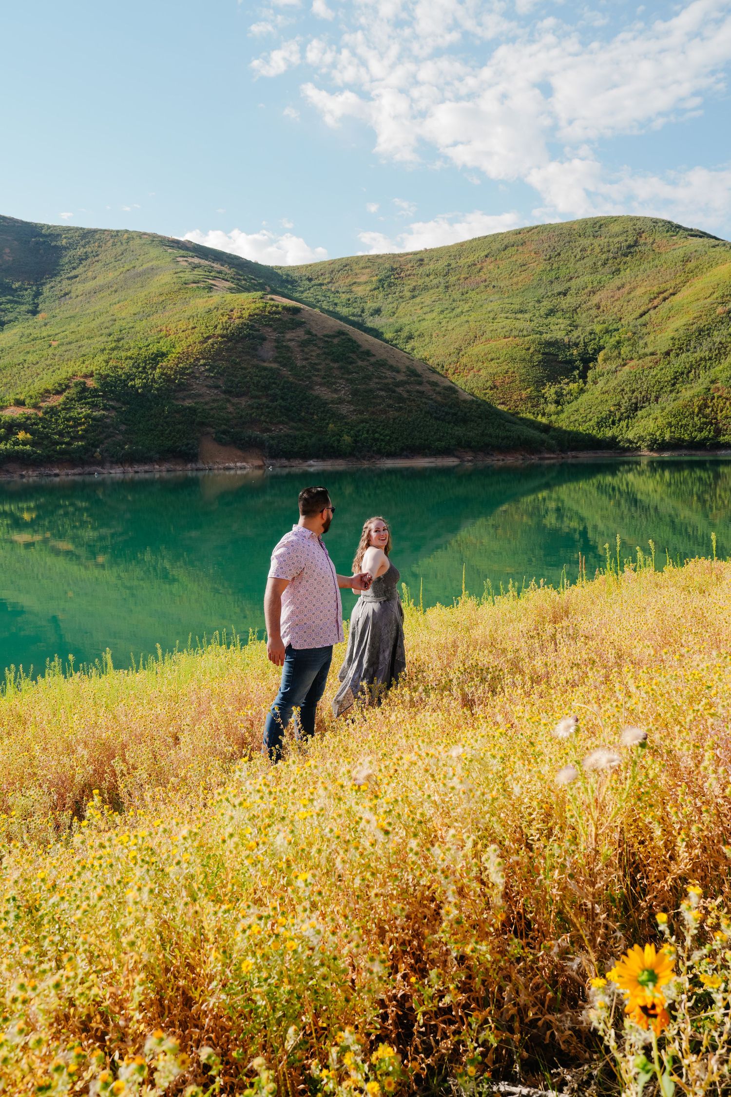 Scenic landscape view of a couple walking through wildflower meadow near turquoise mountain lake.