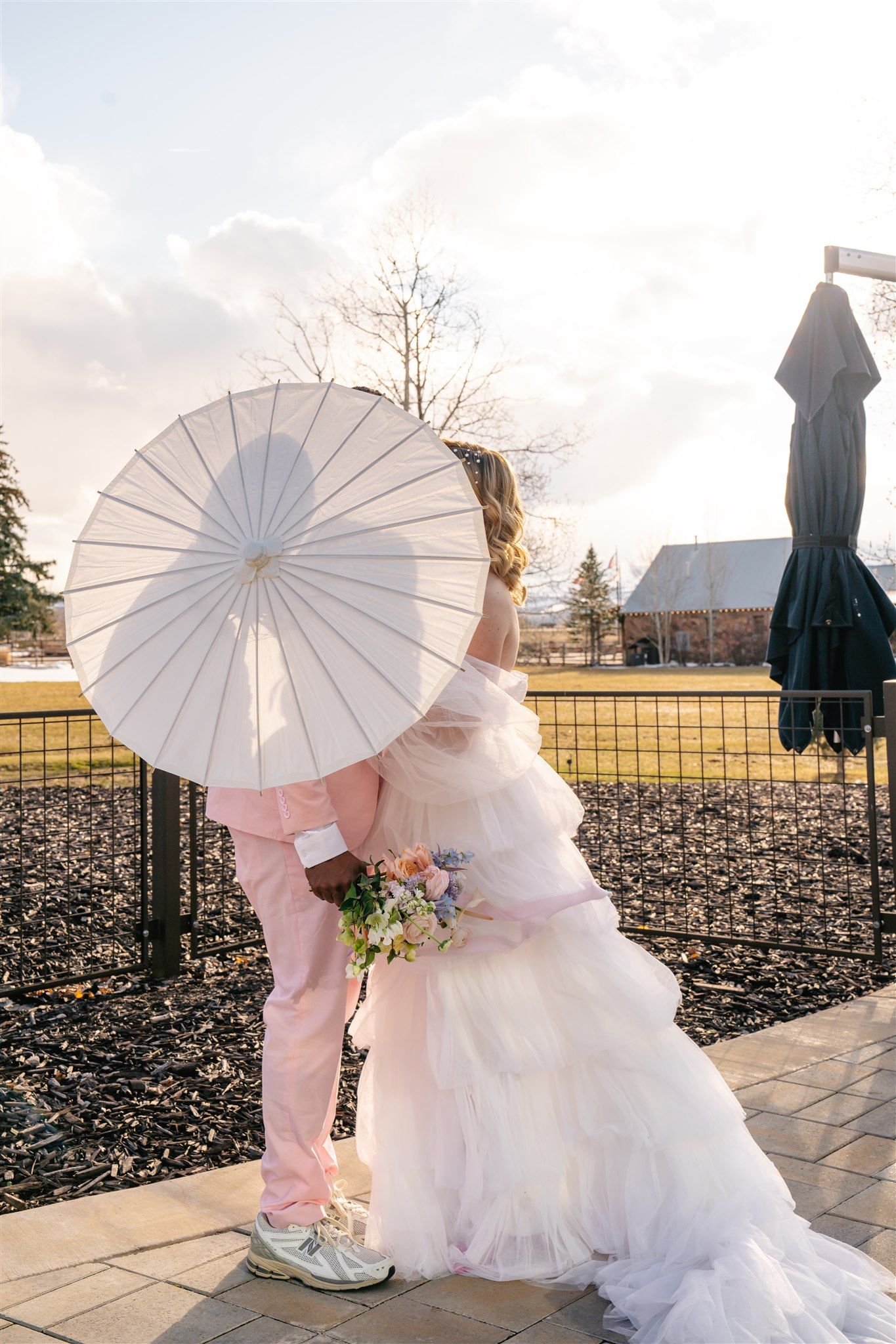 Bride and groom embrace under white parasol with pastel bouquet at Utah wedding venue