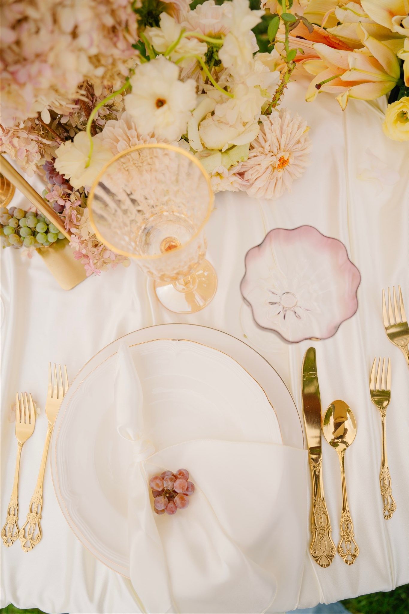 Elegant wedding table setting with white plates, gold flatware and delicate floral arrangements.
