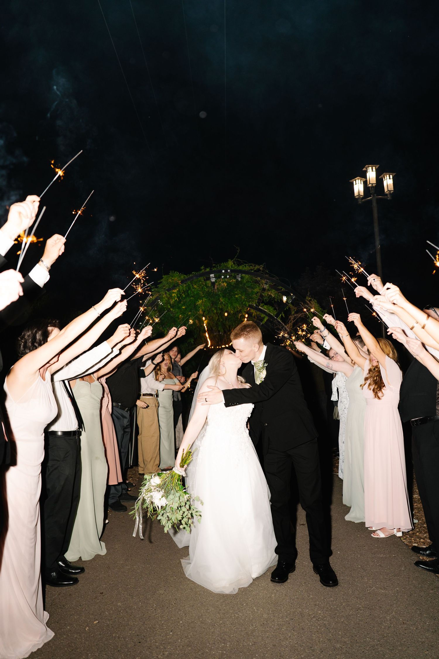 Wedding party holds sparklers creating a magical nighttime exit tunnel for the newlyweds.