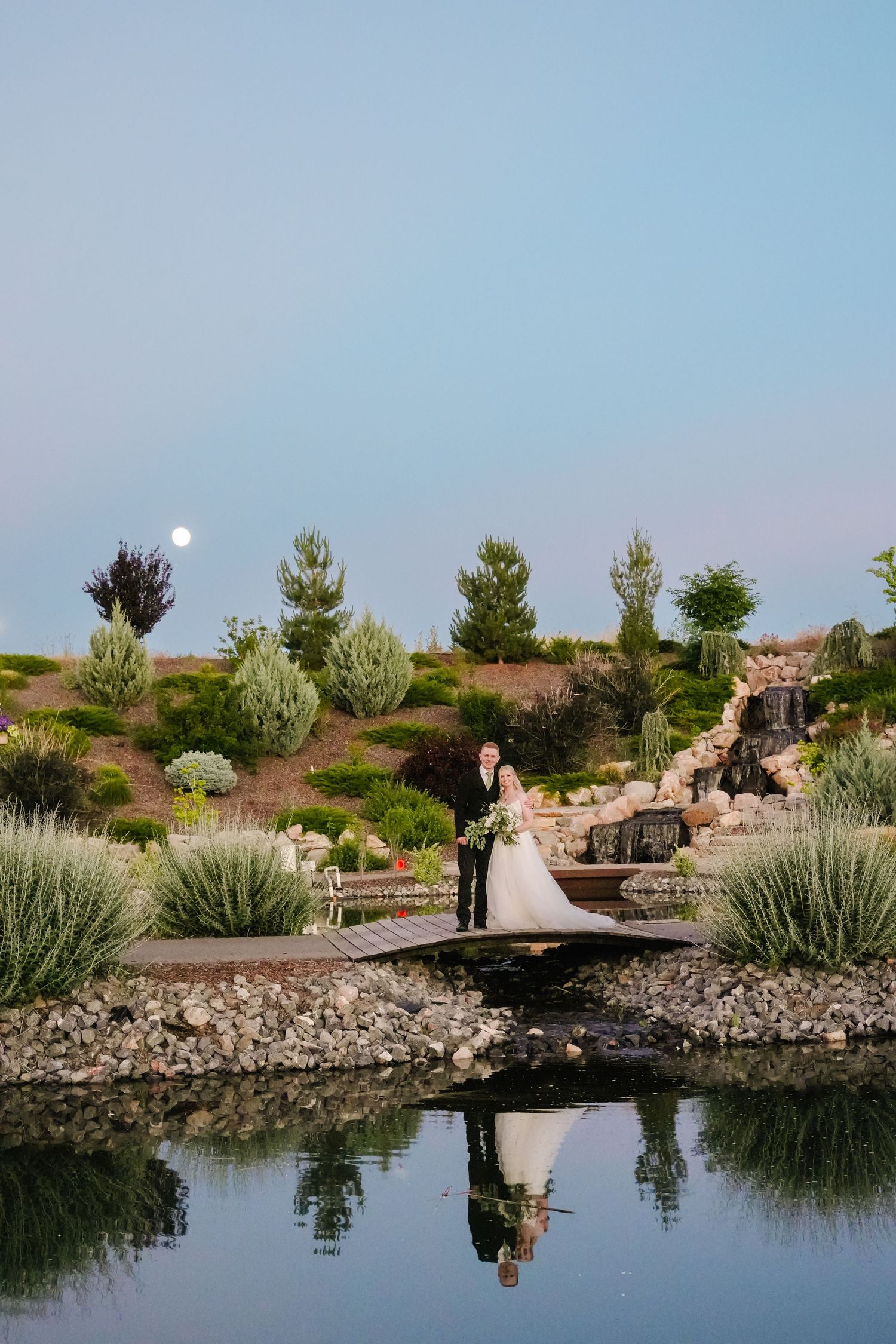 Scenic pond with stone bridge and mountain landscape at sunset.