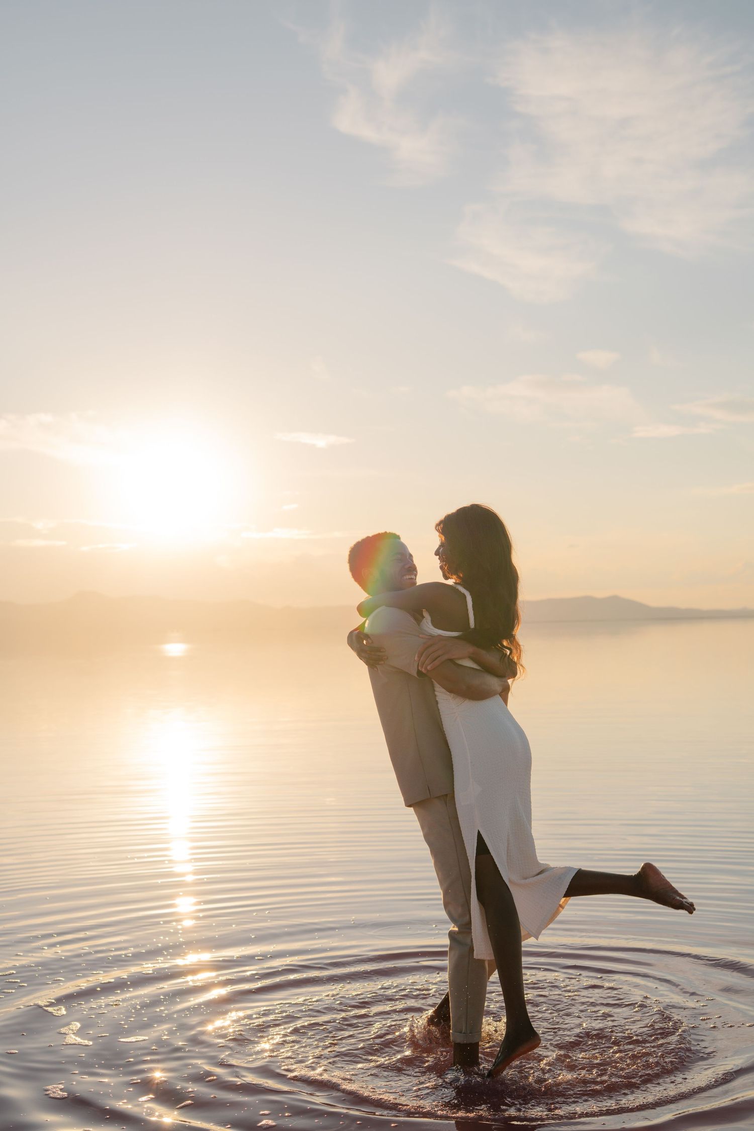 A romantic sunset photoshoot with a couple dancing in shallow water.