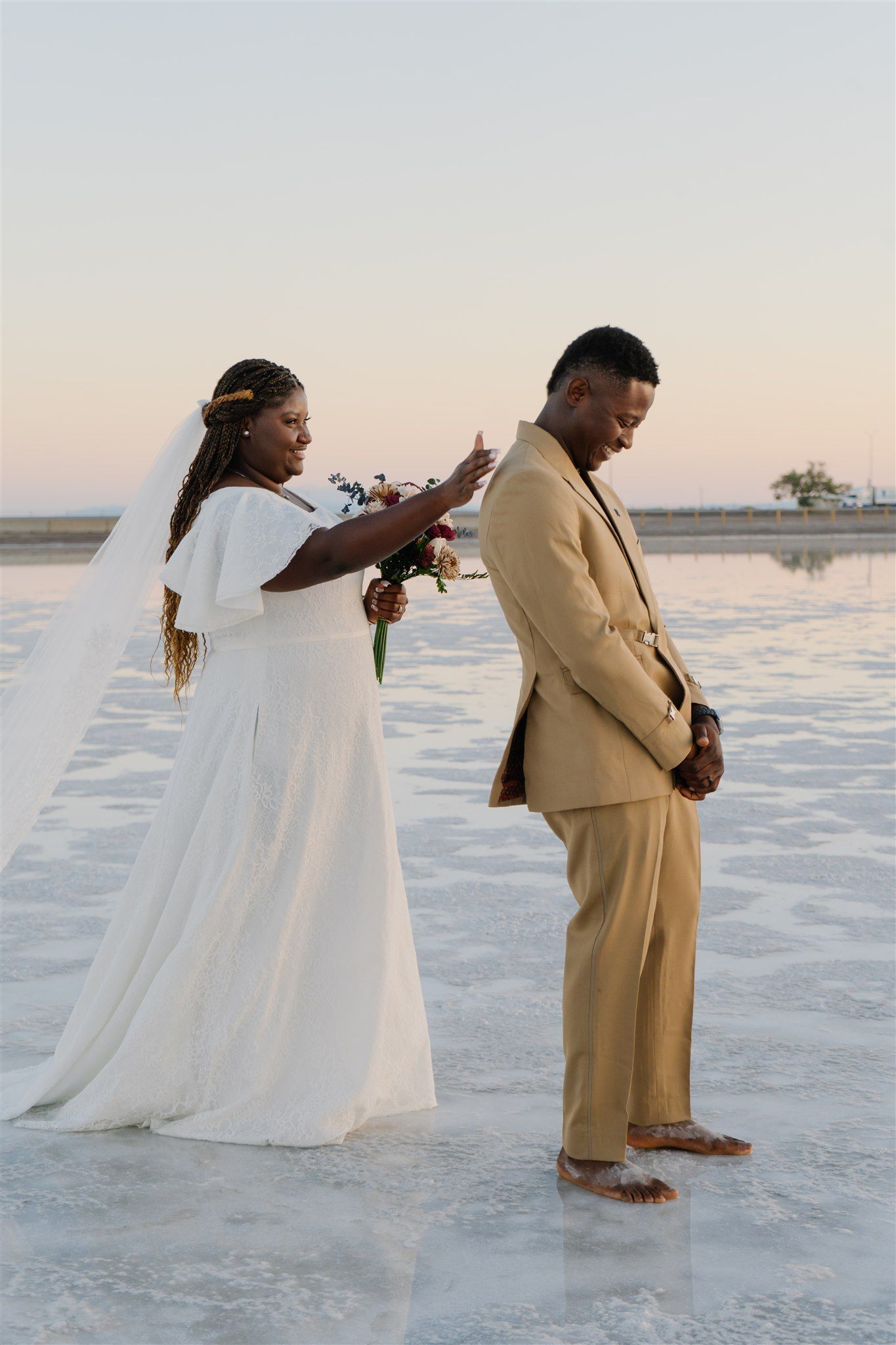 Wedding couple in white dress and tan suit posing on snowy landscape at sunset.