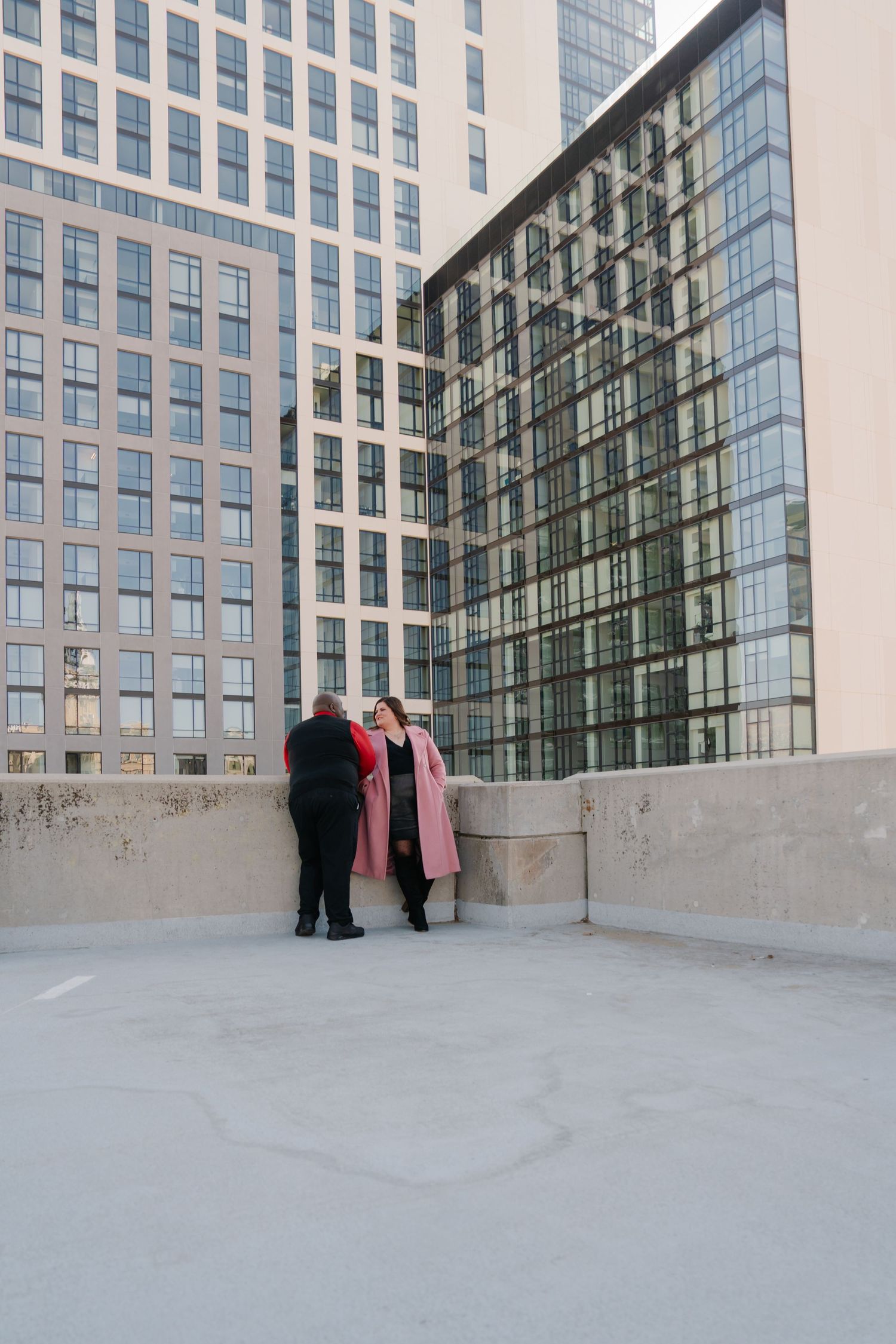 Two people stand near a modern glass office building on an urban rooftop.