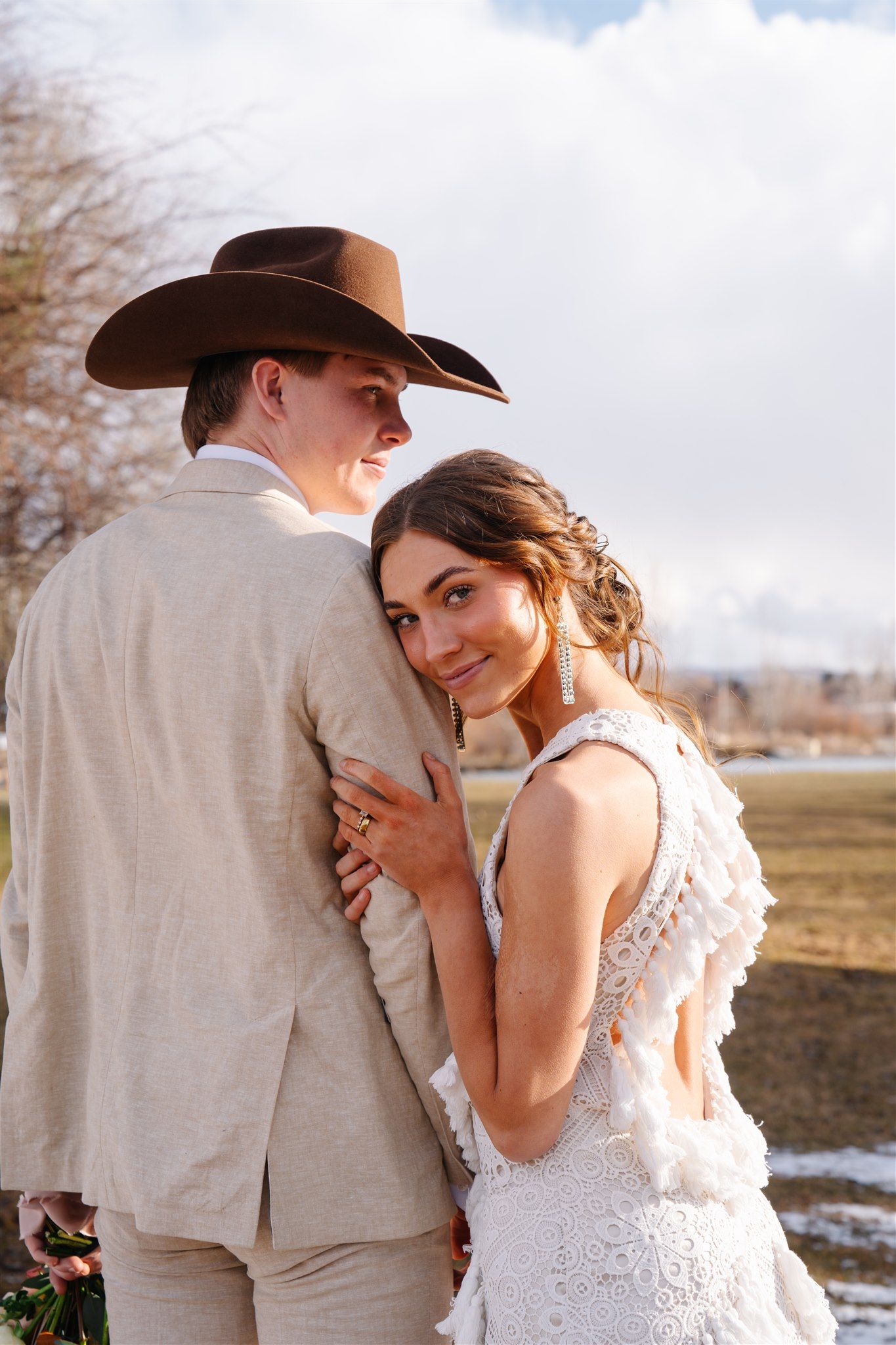 A romantic outdoor wedding scene with a couple in western attire embracing in a field.