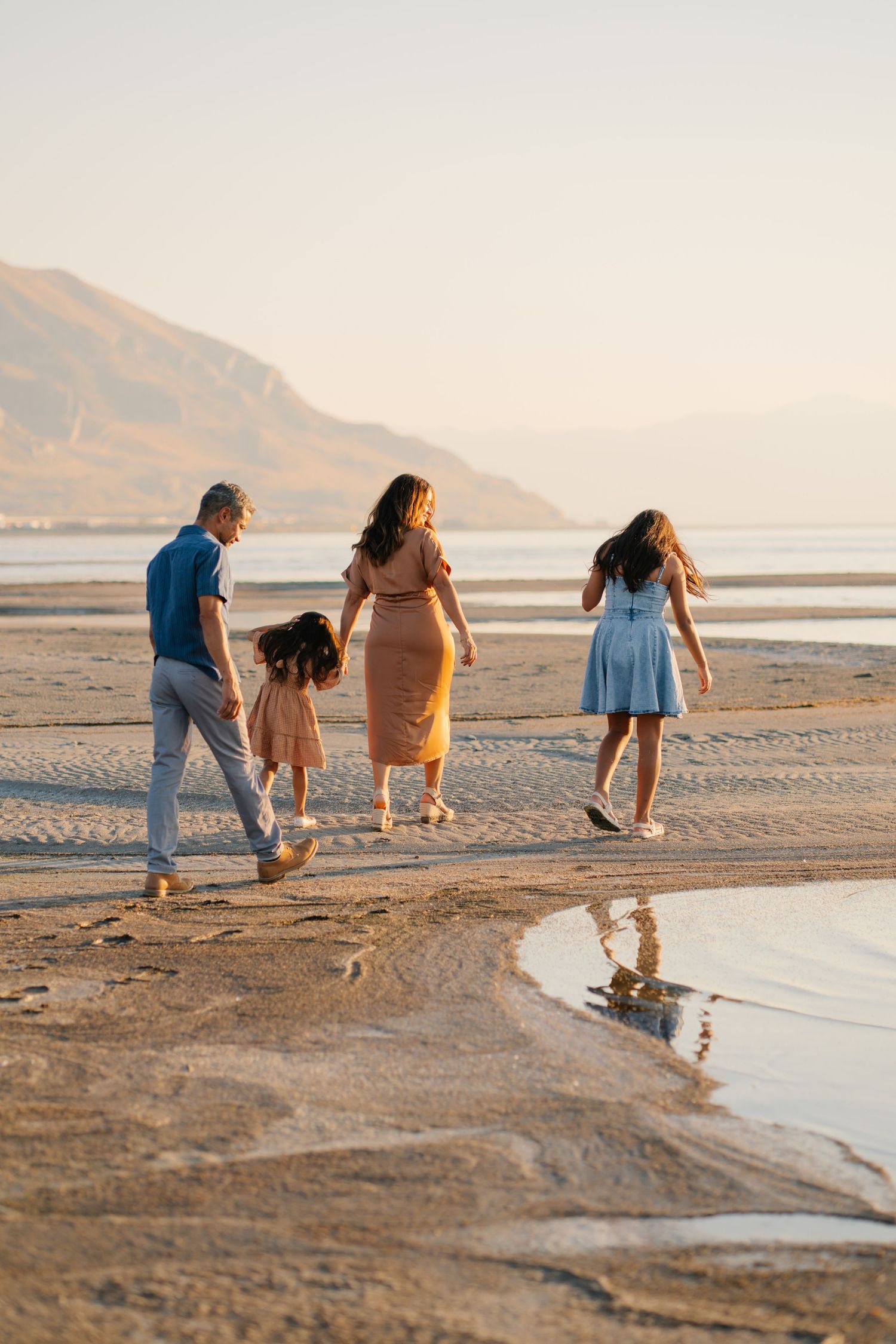 Family of four walking on a sandy beach at sunset with mountains in the background.
