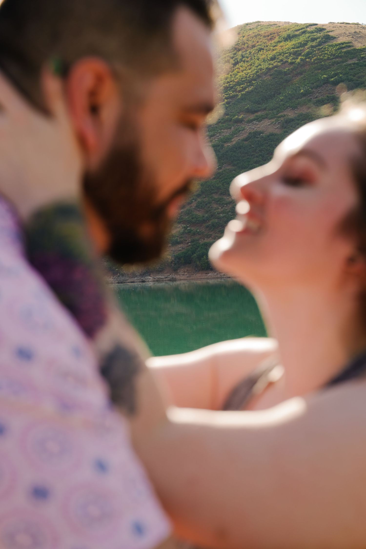 Intimate close-up of a couple about to kiss with mountains and lake in background.