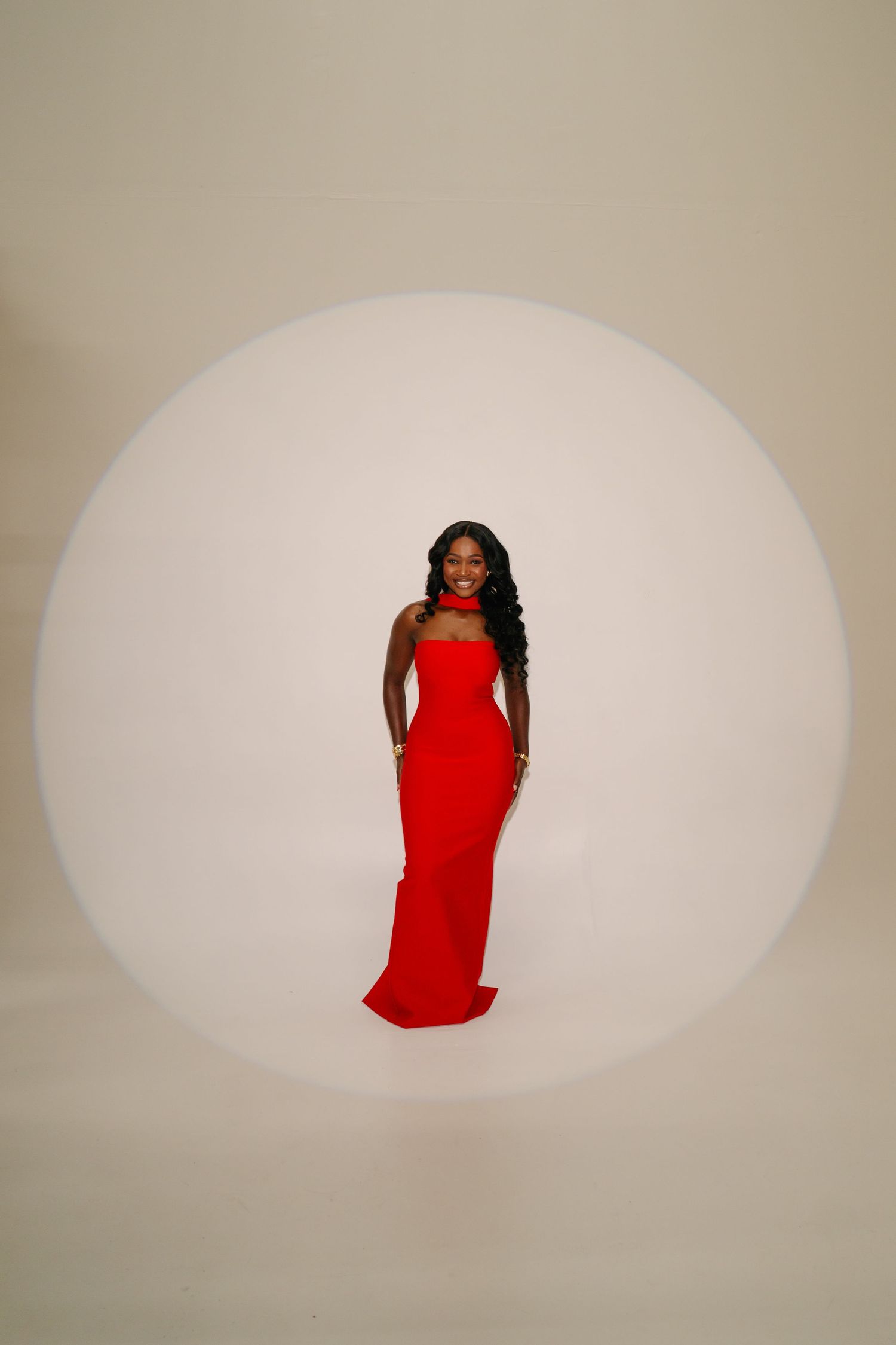 A figure in a red dress poses elegantly against a minimalist white backdrop.