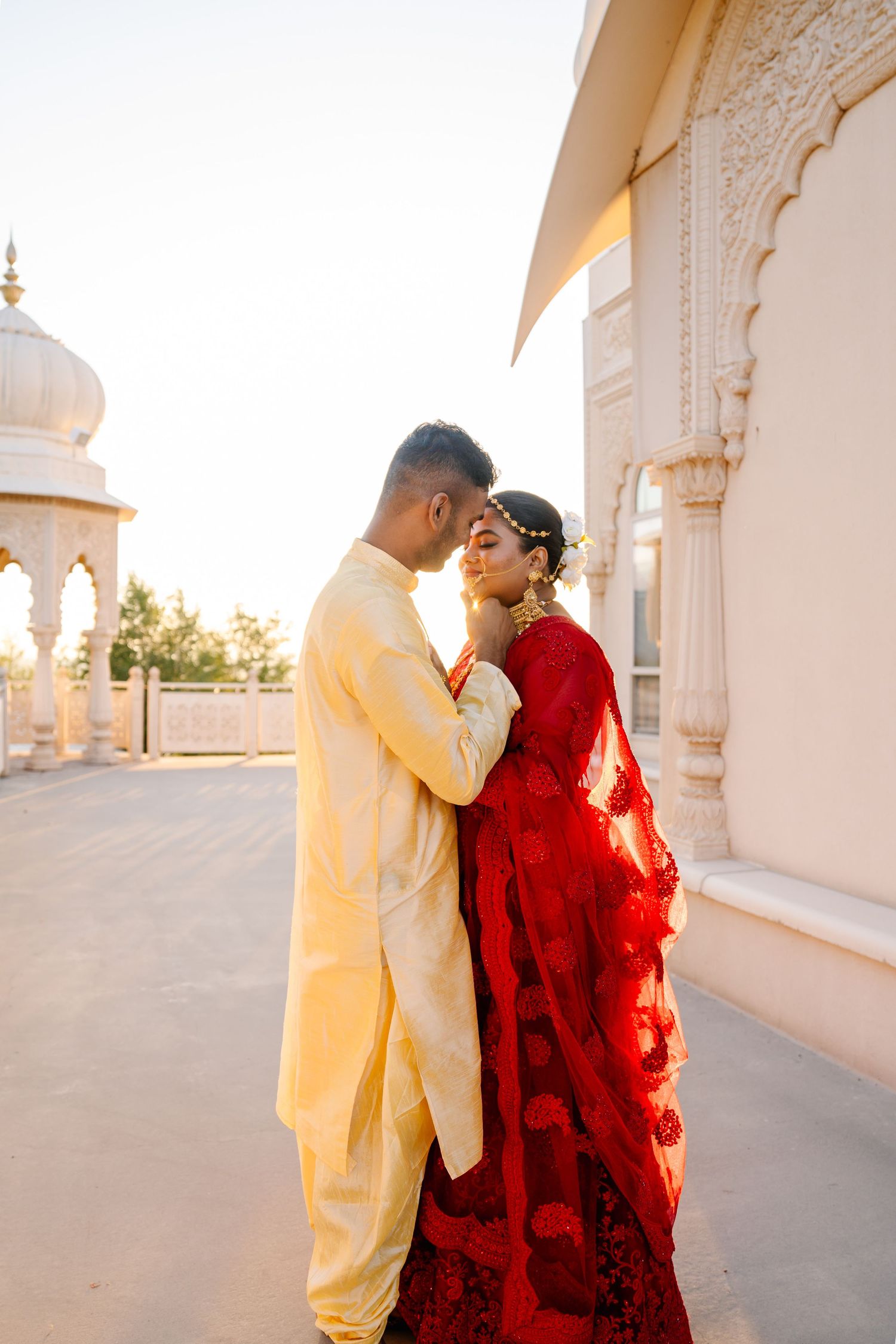 A couple shares intimate moments in traditional Indian wedding attire at a marble pavilion.