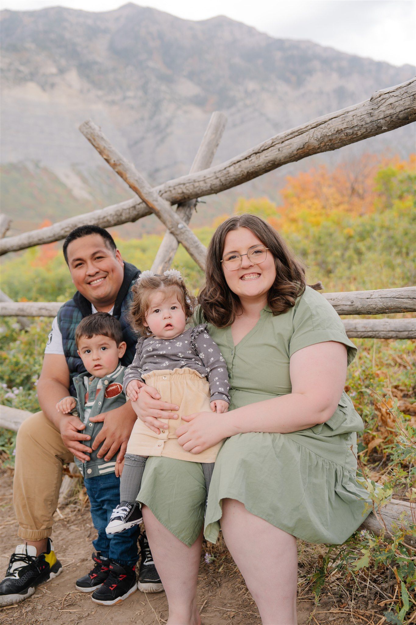 Family sitting together on rustic wooden fence with mountain landscape in background.